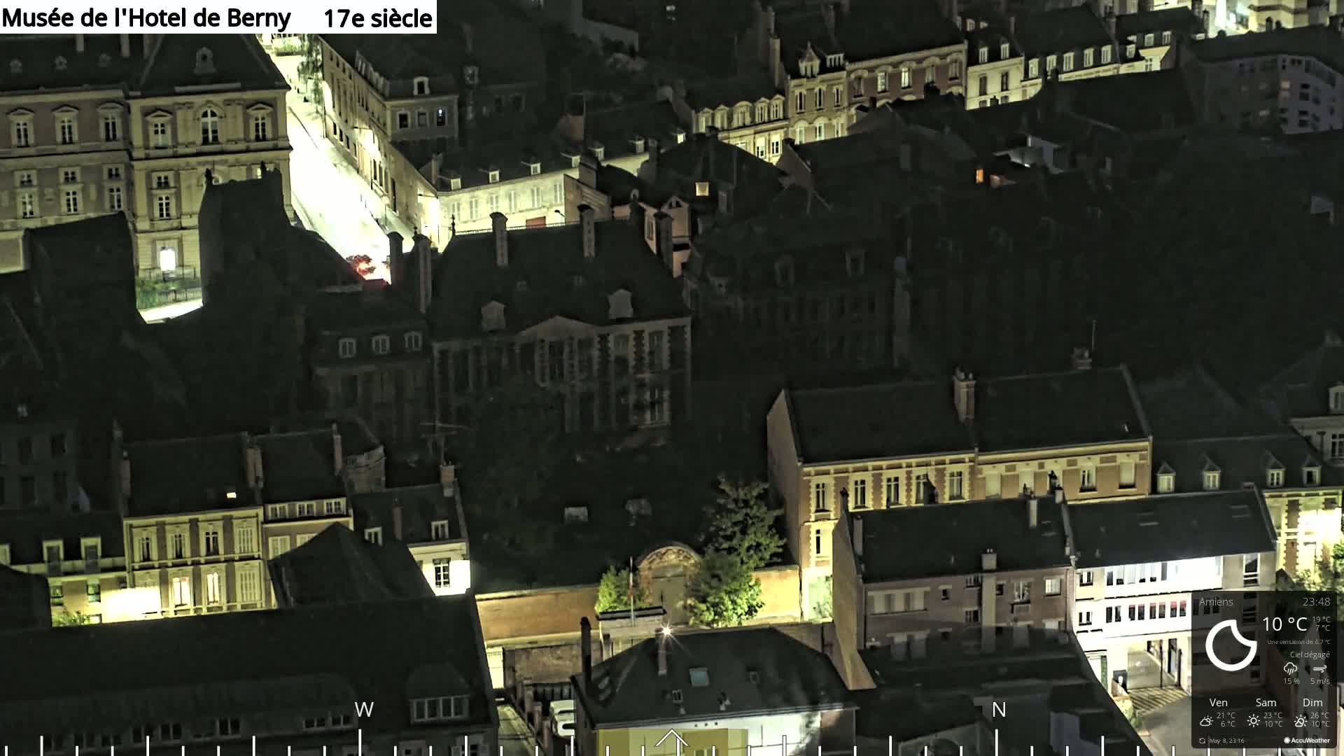 A nighttime, high-angle view of a European city, showing many buildings with illuminated windows and a clear sky.