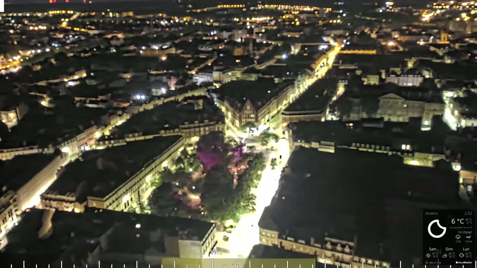 An aerial nighttime view of a city with brightly lit streets and buildings, under a clear sky.