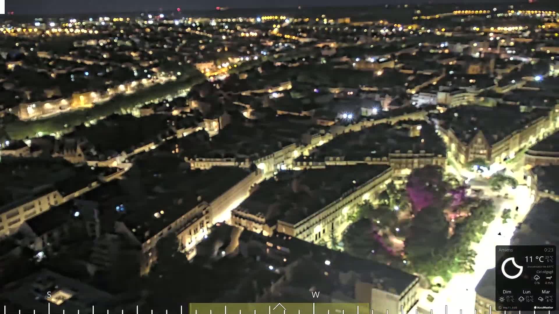 A nighttime aerial view of a city with brightly lit streets and buildings under a clear sky.