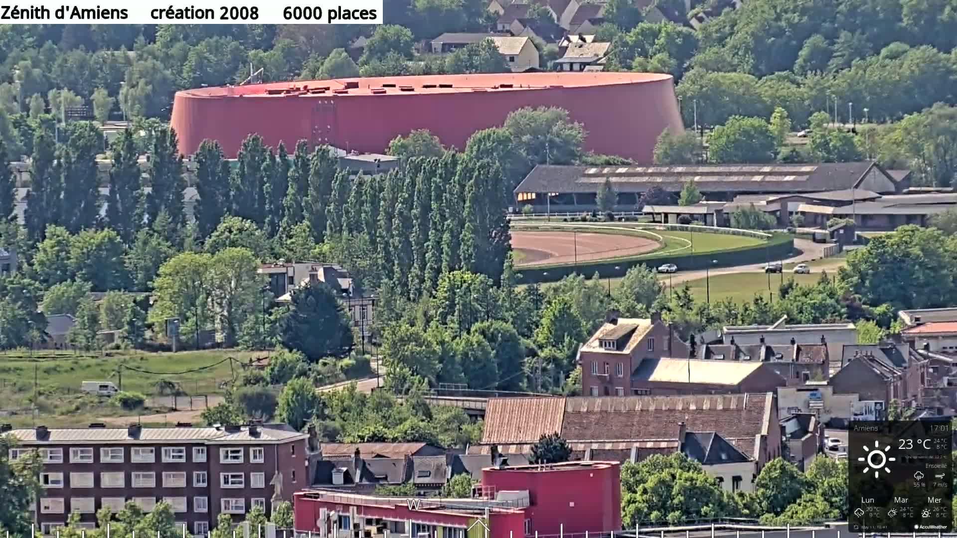 A large red building sits beside a racetrack in a sunlit city landscape.