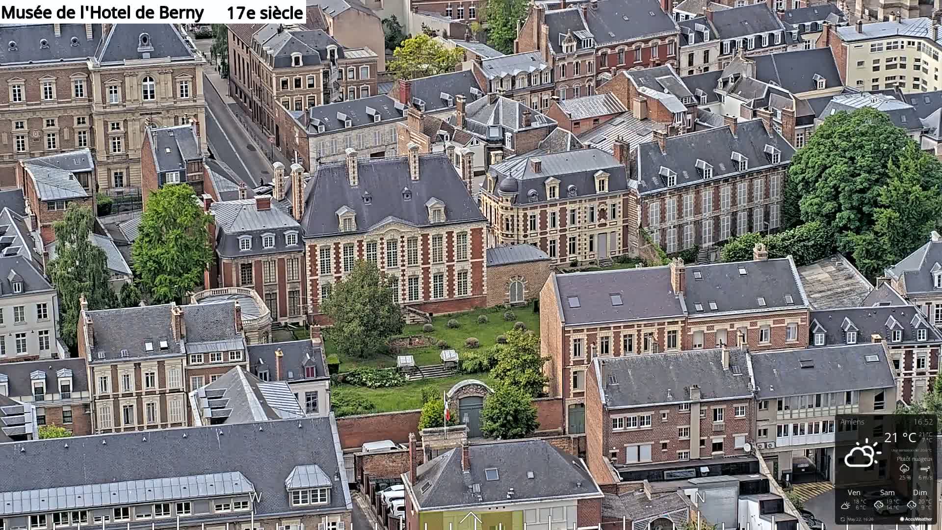An aerial view of a European city on a partly cloudy day shows a large, multi-story building surrounded by smaller, similarly styled buildings.