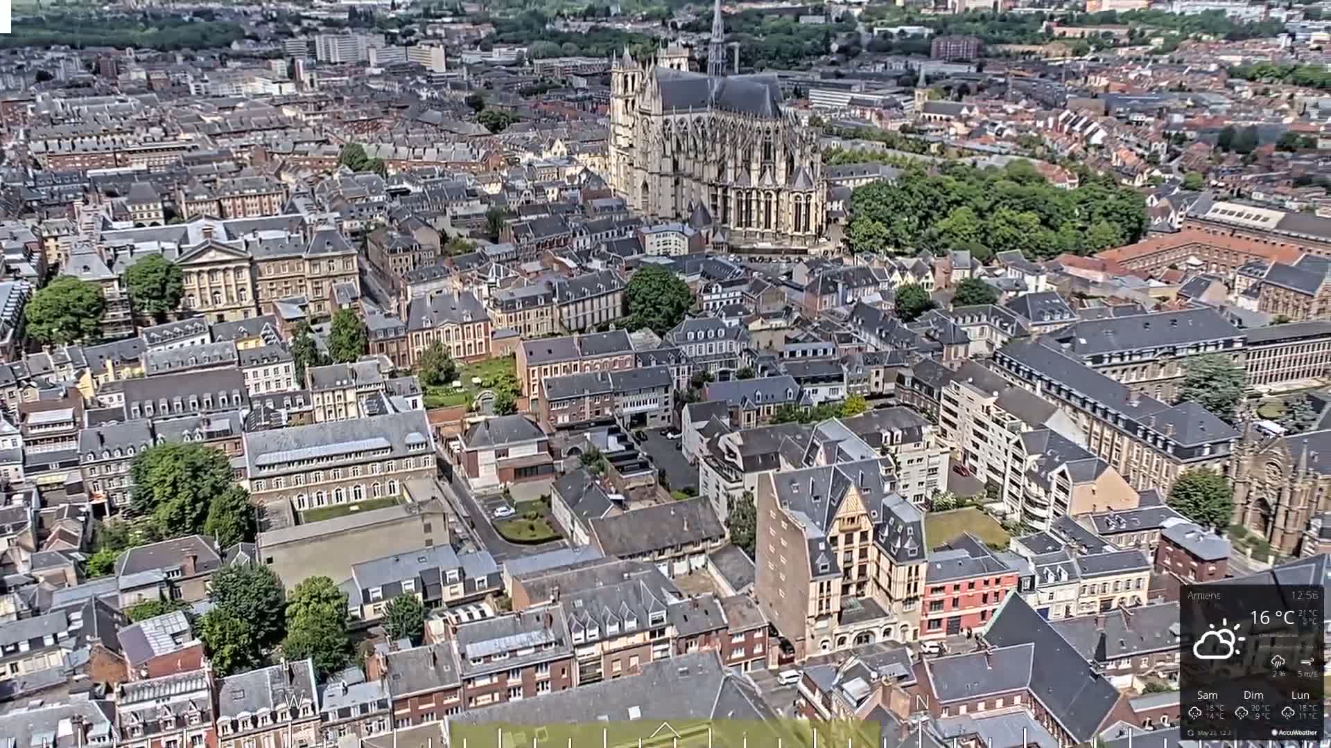 A high-angle view of a dense European city on a partly cloudy day, showcasing a large cathedral at its center.