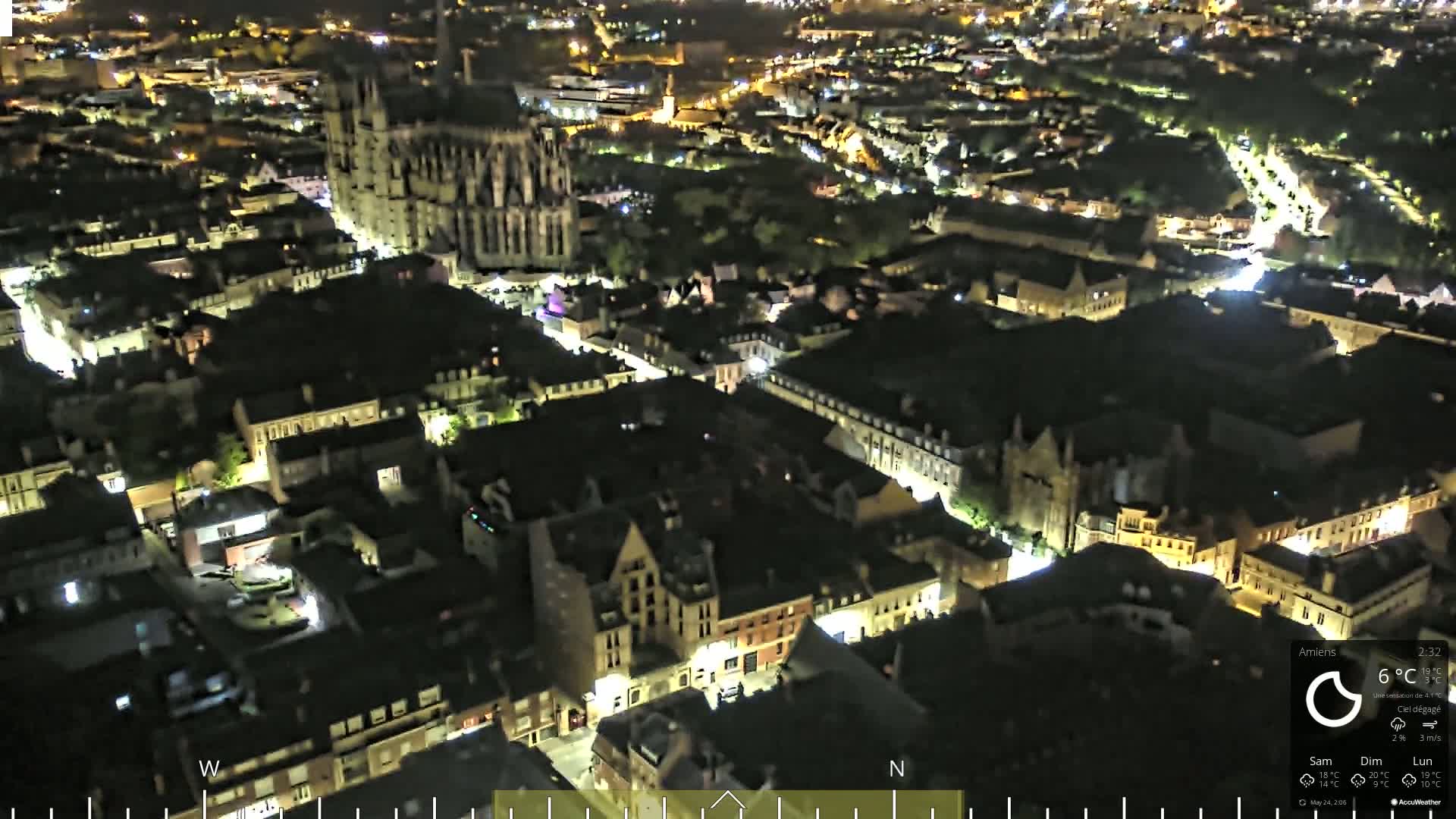 A nighttime aerial view of a city with a large cathedral at its center, under a clear sky.
