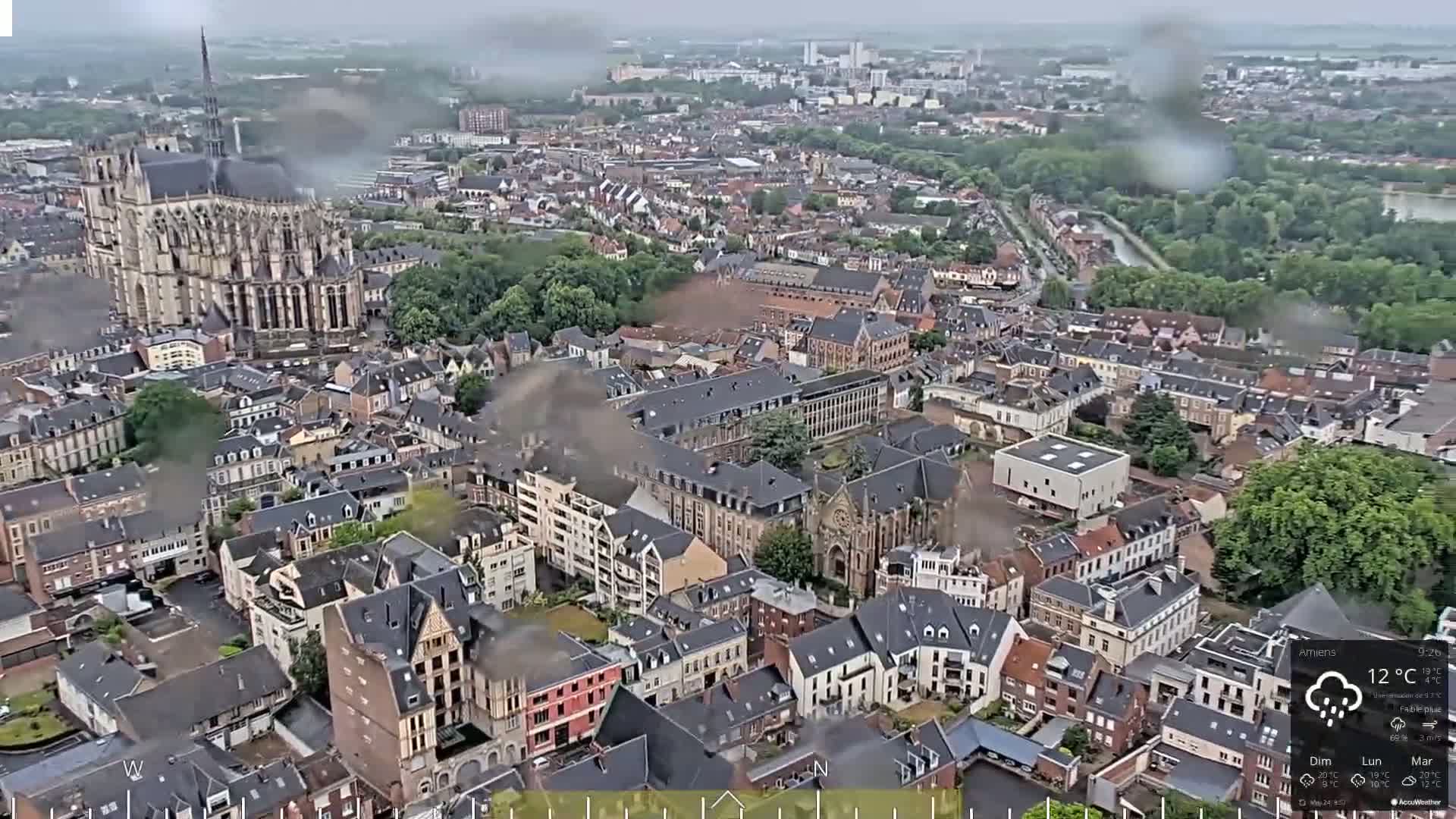 A rain-soaked aerial view shows a European city with a large cathedral and many closely-packed buildings.