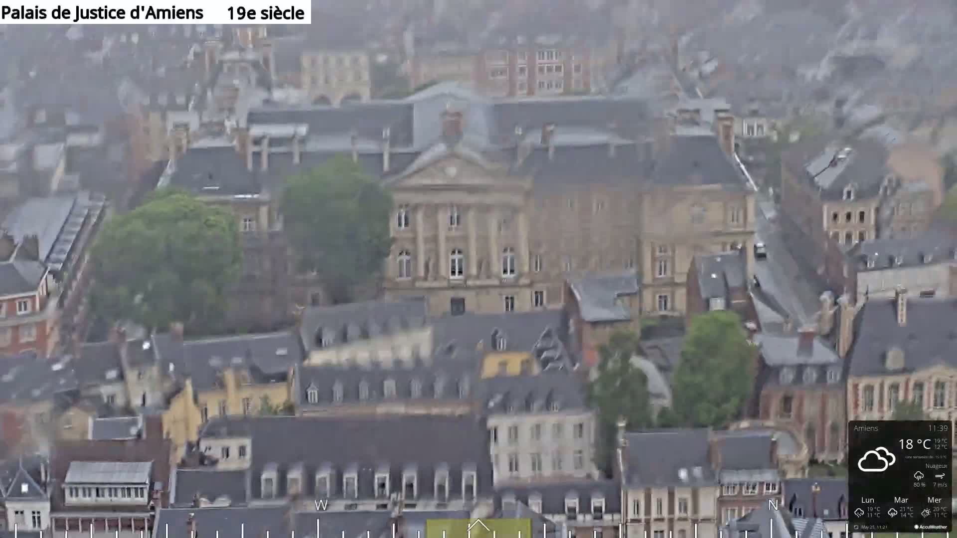 A high-angle, long shot of a European city on an overcast day shows many buildings, with one large building in the center.