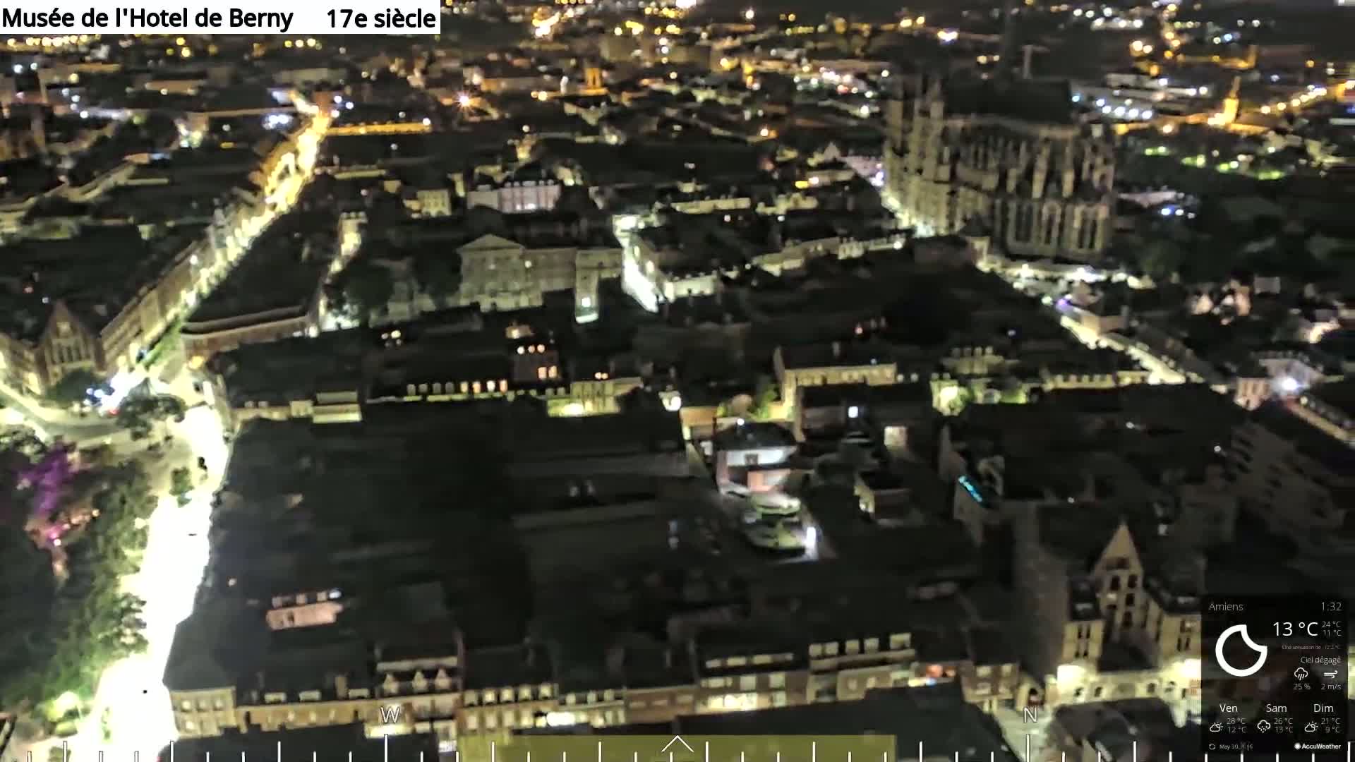 A nighttime aerial view of a city with illuminated streets and buildings, including a large cathedral, under clear skies.