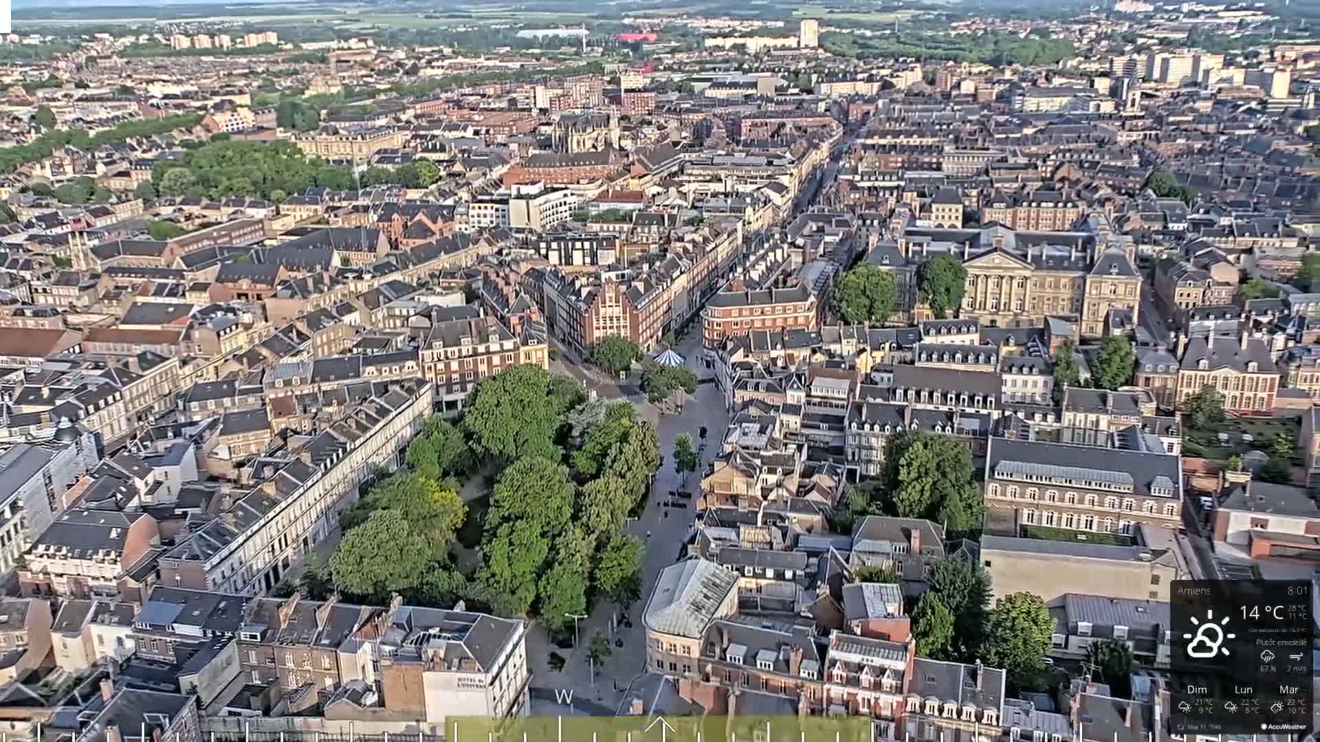 A high-angle, sunny view of a European city with densely packed buildings and a central green space.