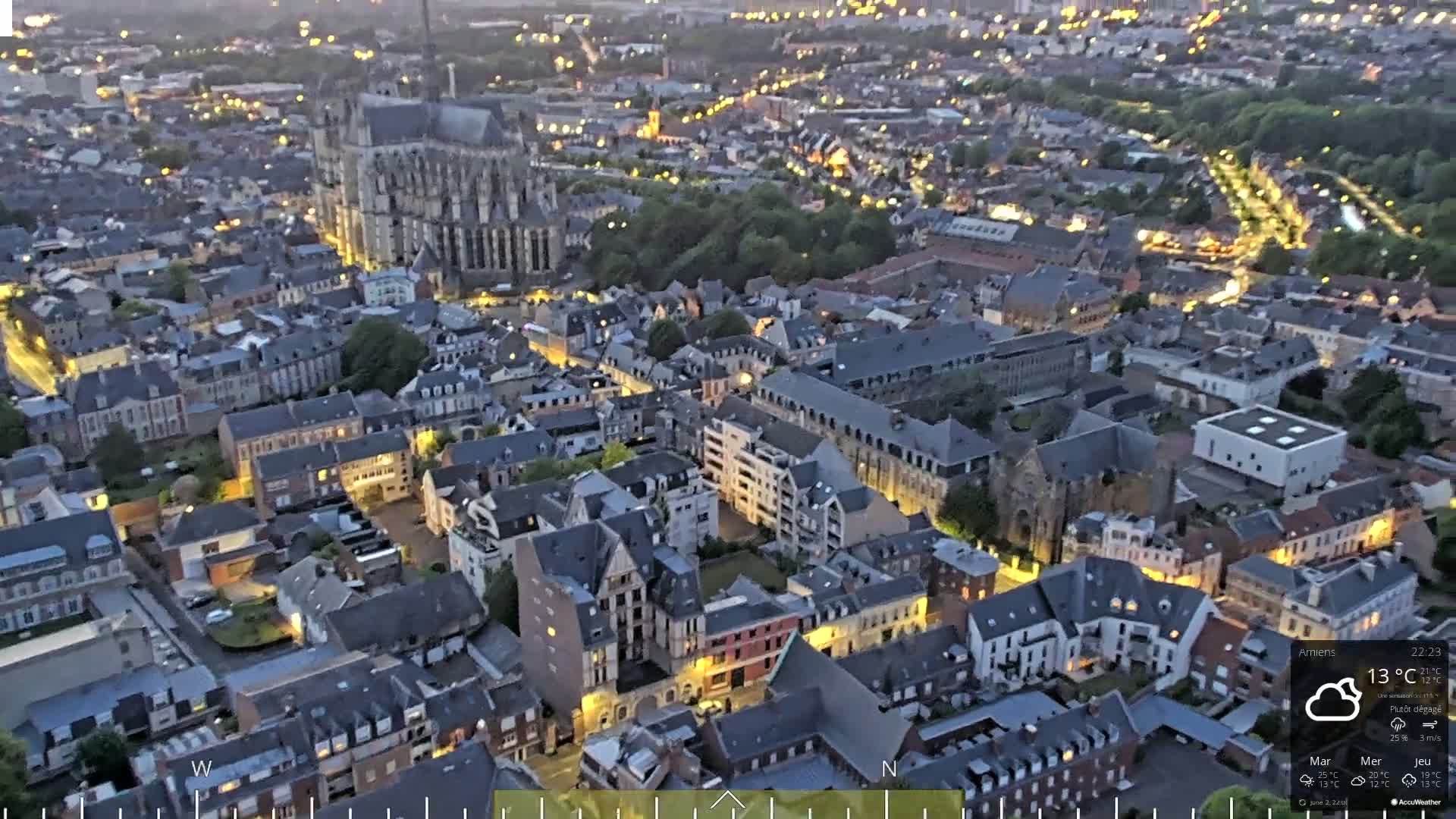 A nighttime aerial view of a European city with a large cathedral, showing many illuminated buildings under a partly clear sky.