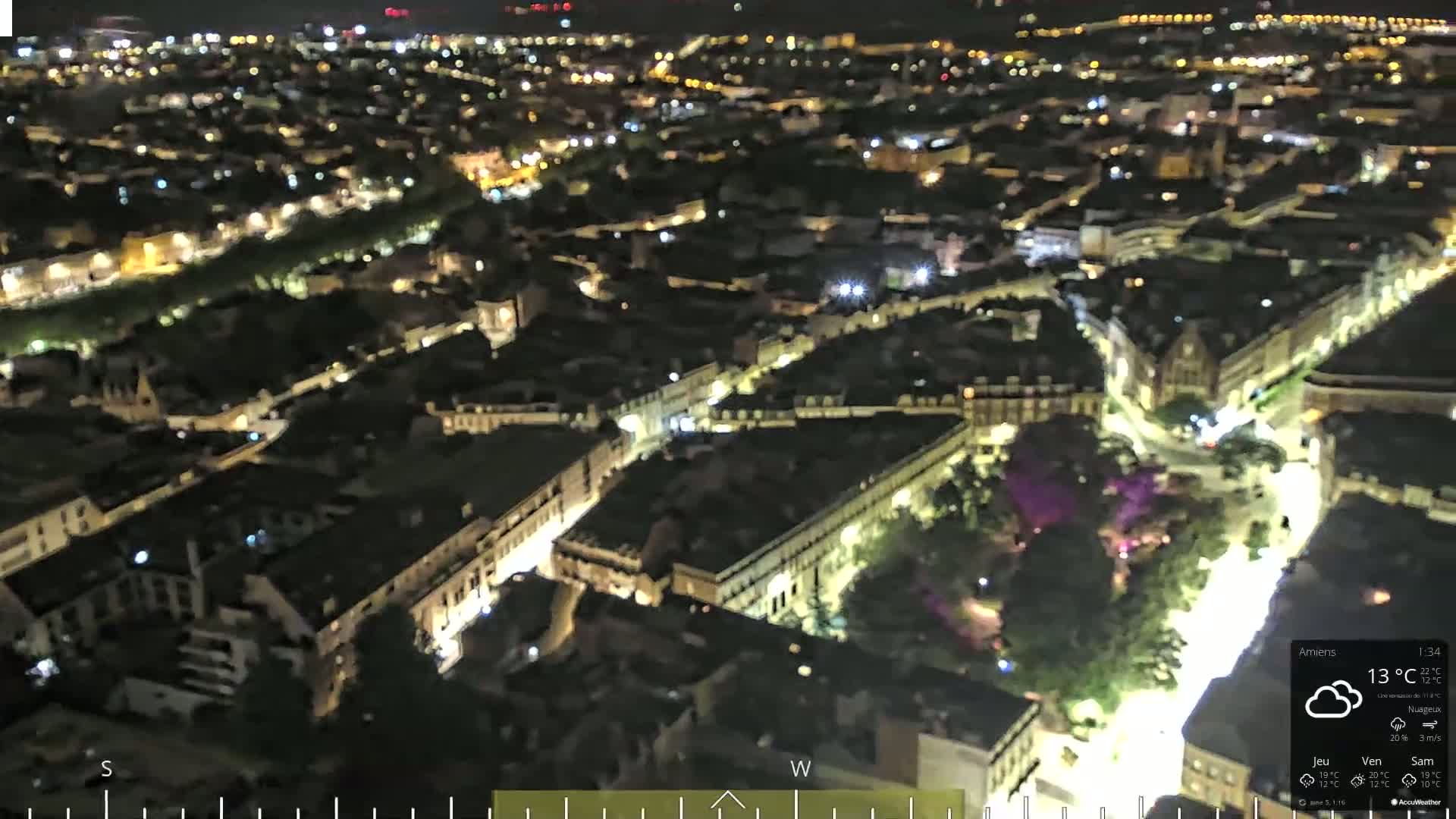 A nighttime aerial view of a city, showing illuminated streets and buildings under cloudy skies.
