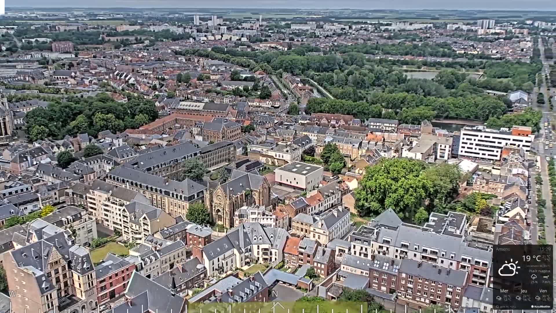 An aerial view of a densely packed European city on a partly cloudy day, showing a mix of residential buildings and some larger structures.