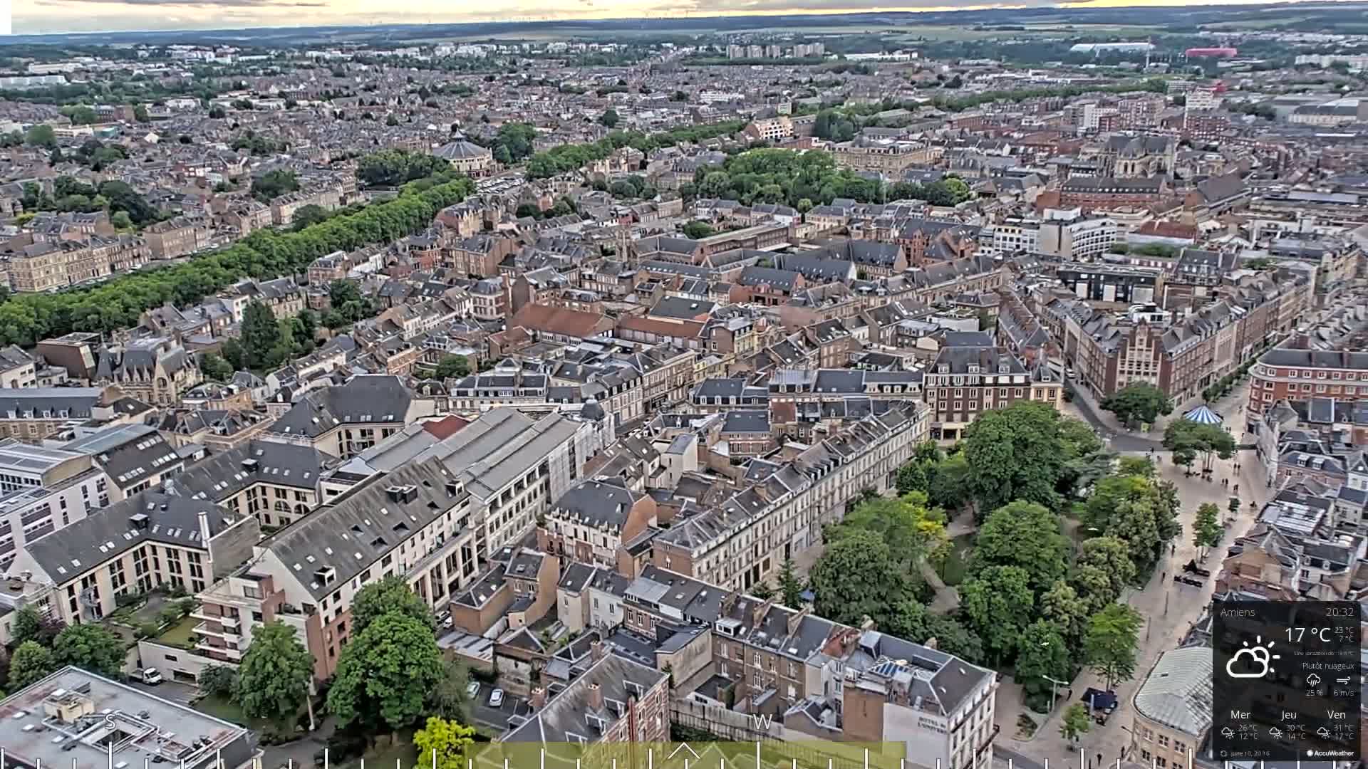 An aerial view of a European city on a partly cloudy day, showing densely packed buildings and a central park.