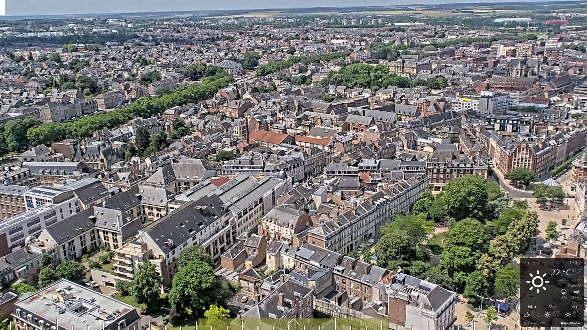 A high-angle, sunny view of a densely populated European city with many closely-packed buildings and a large green park.