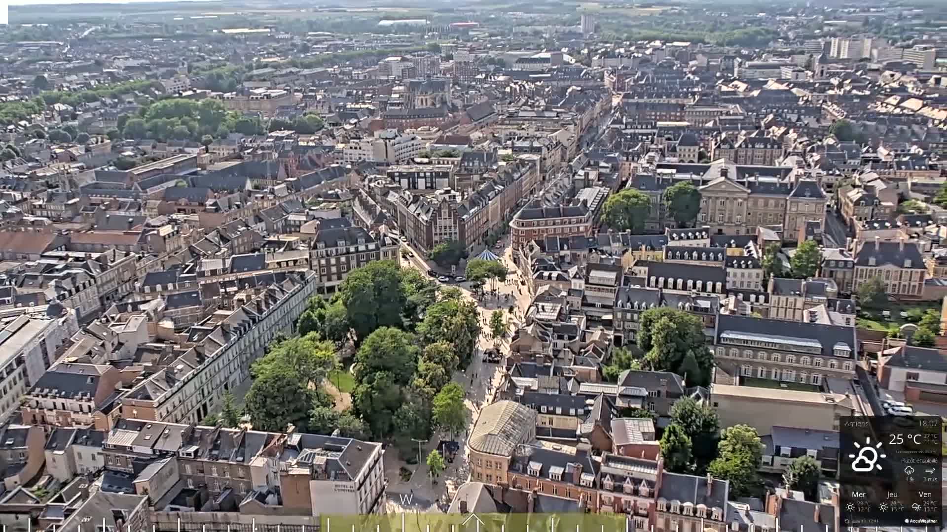 A high-angle, long shot of a city on a mostly sunny day shows many buildings and green spaces.
