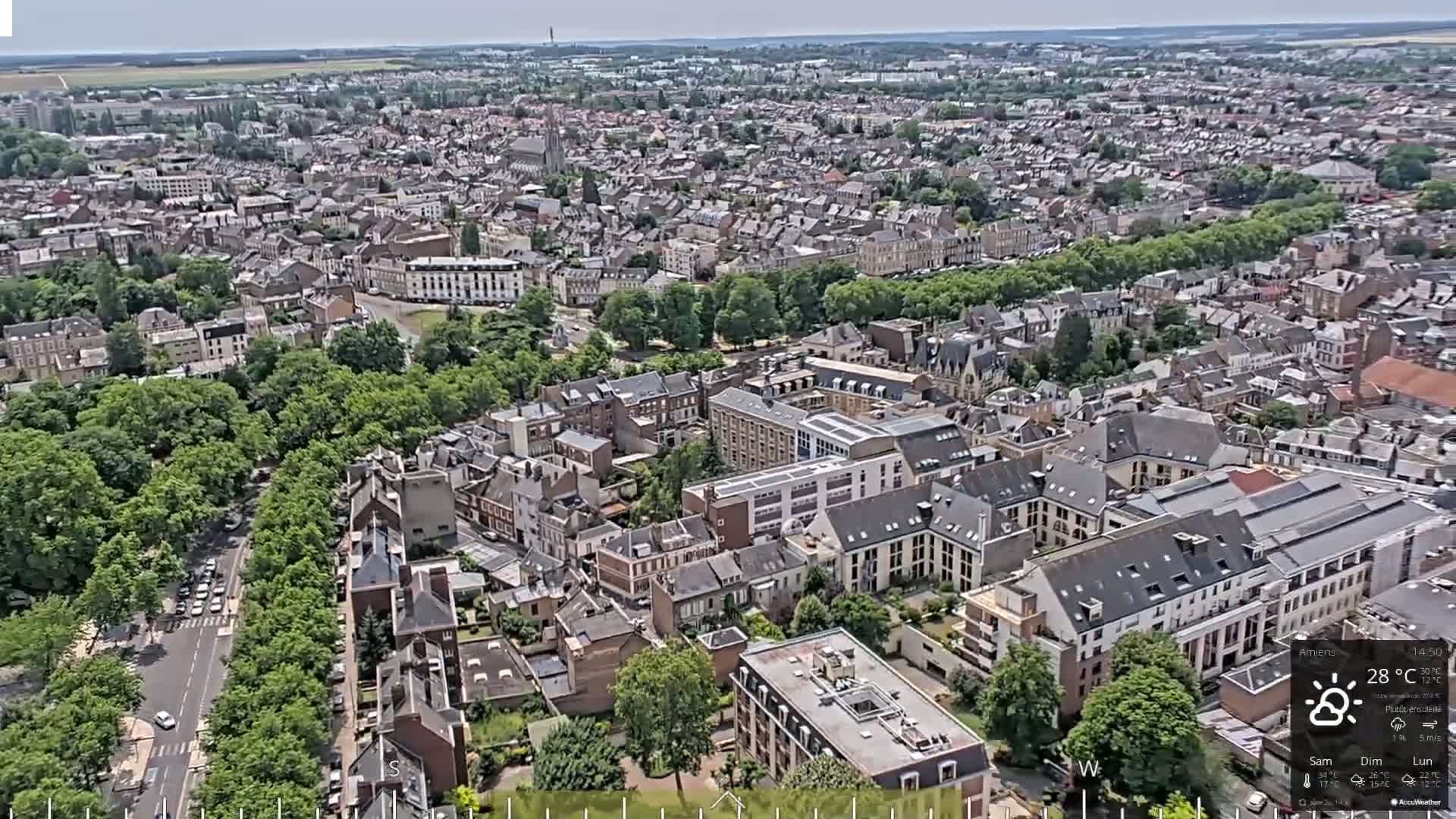 A high-angle, sunny view of a densely populated city with many trees and buildings.