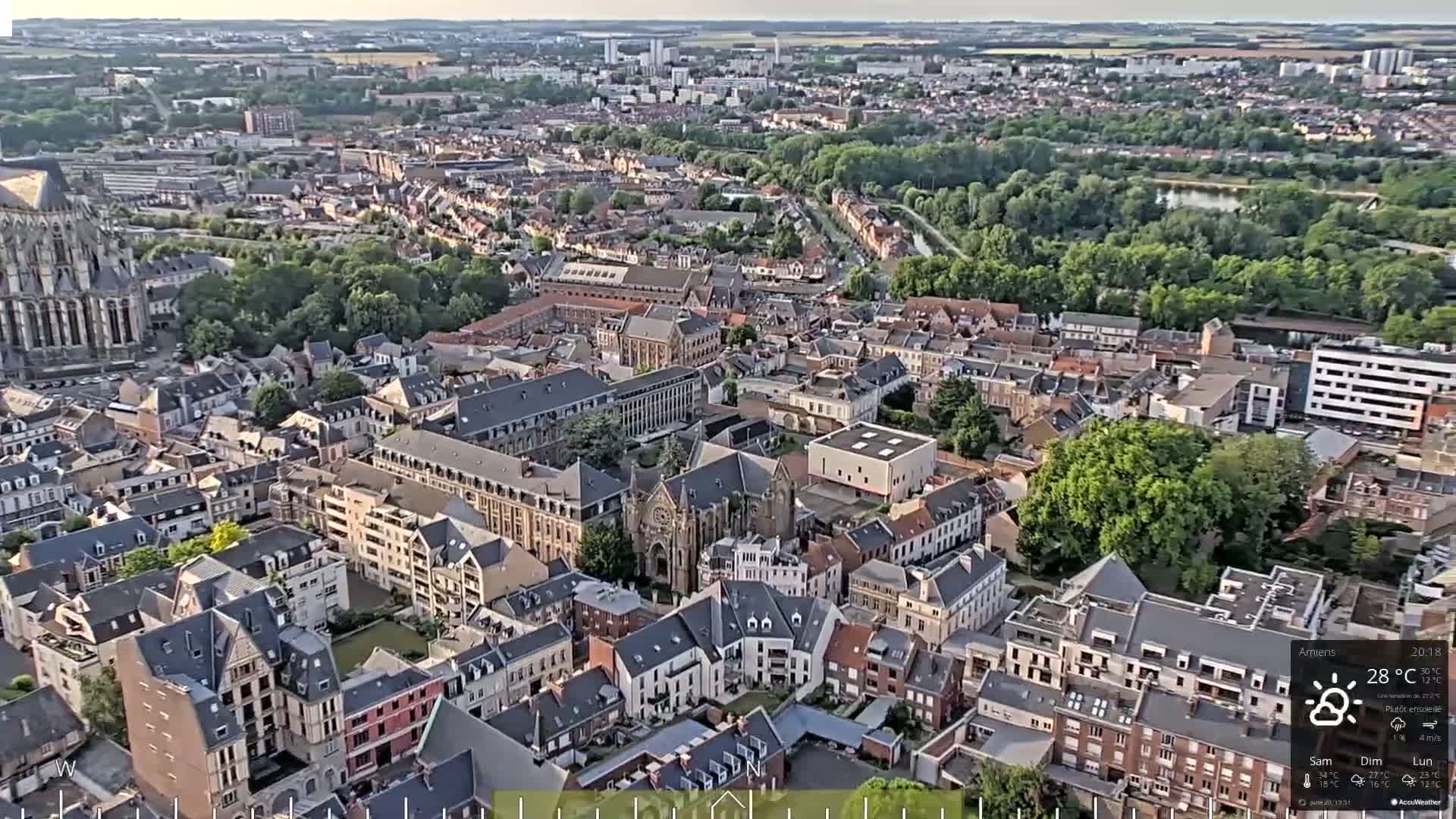 An aerial view of a European city on a mostly sunny day, showing a dense collection of buildings with a large cathedral in the background.