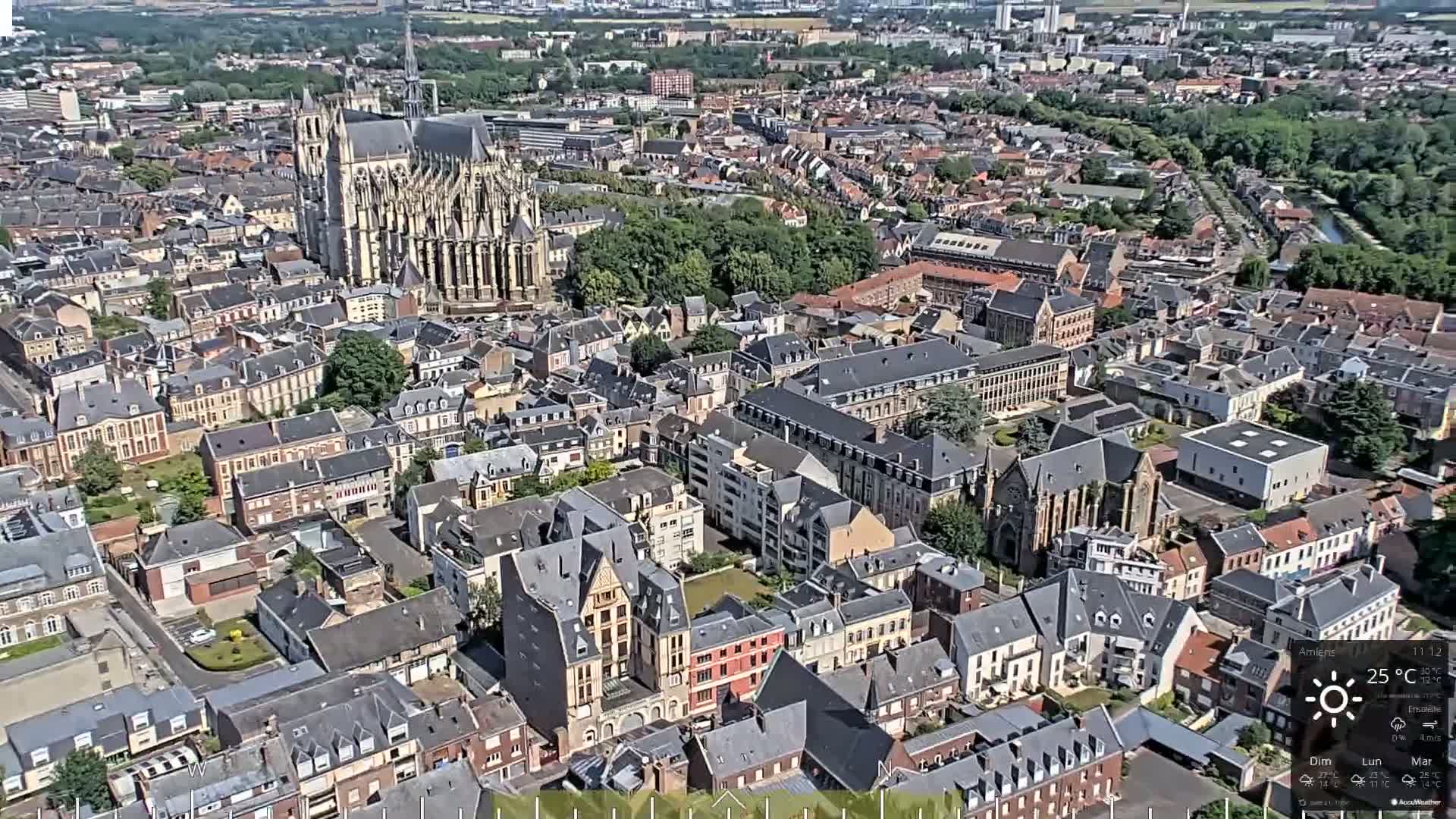 An aerial view of a European city on a sunny day shows a large cathedral and many closely packed buildings.