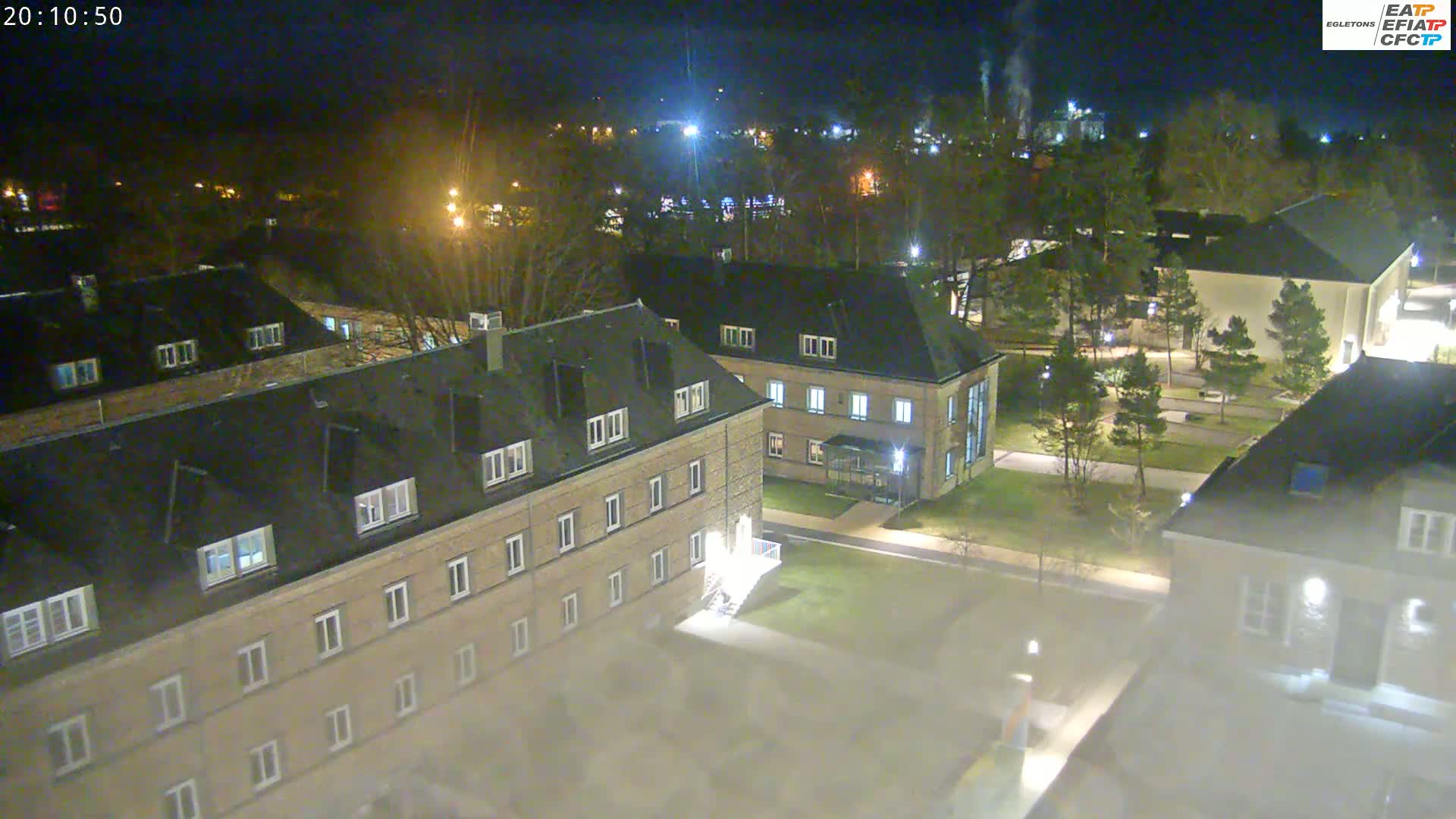 A nighttime aerial view of a campus with several low-rise buildings, trees, and pathways shrouded in a light fog.