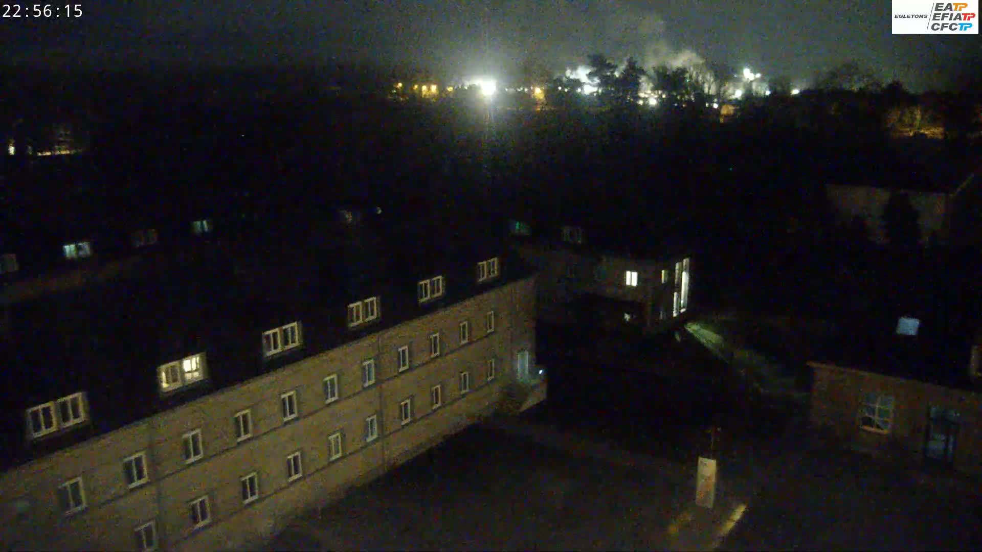 A nighttime aerial view shows a complex of buildings with some lights on, under a dark, clear sky.