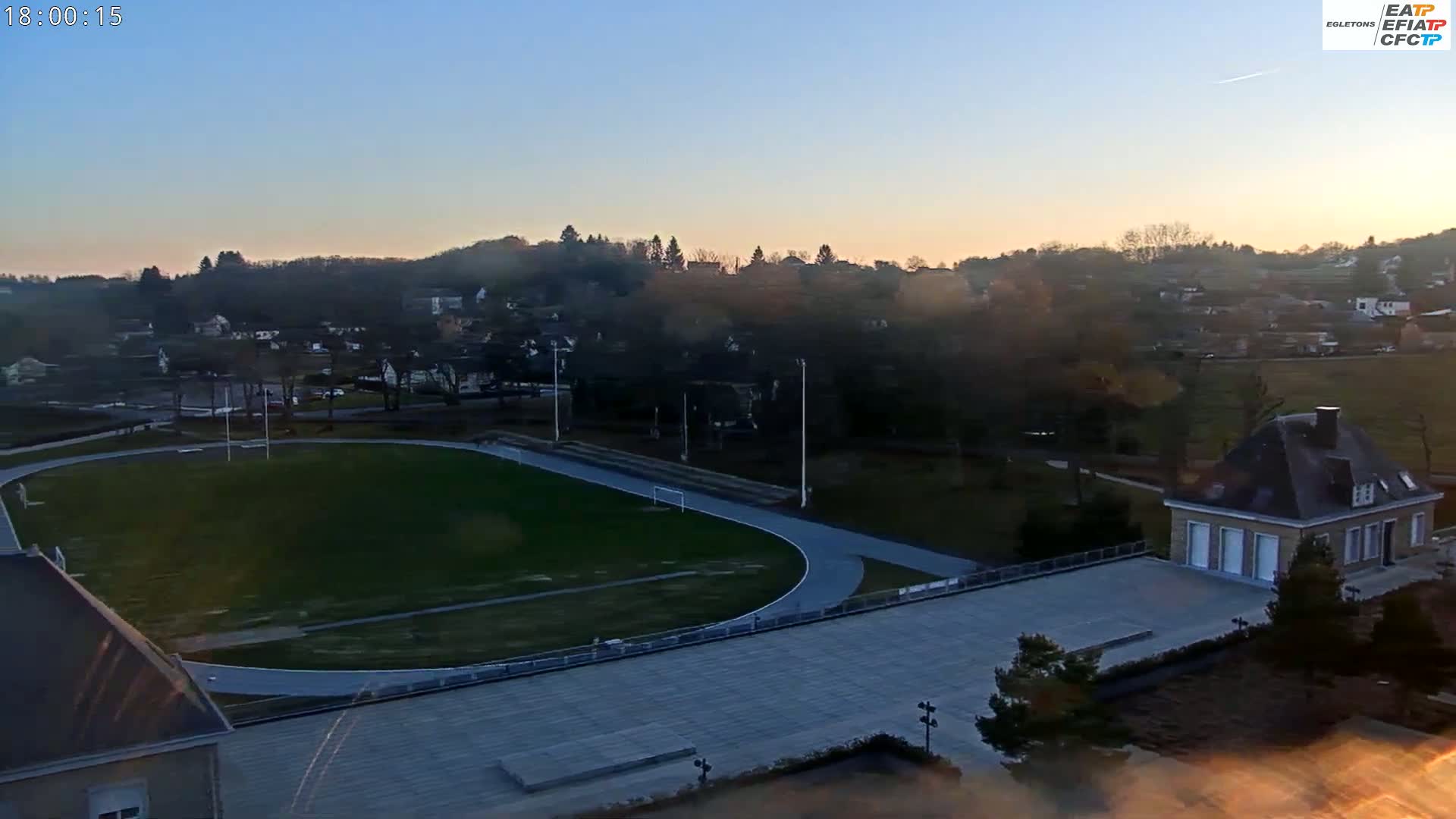 An aerial view shows a running track and soccer field next to a small building at sunset under a clear sky.