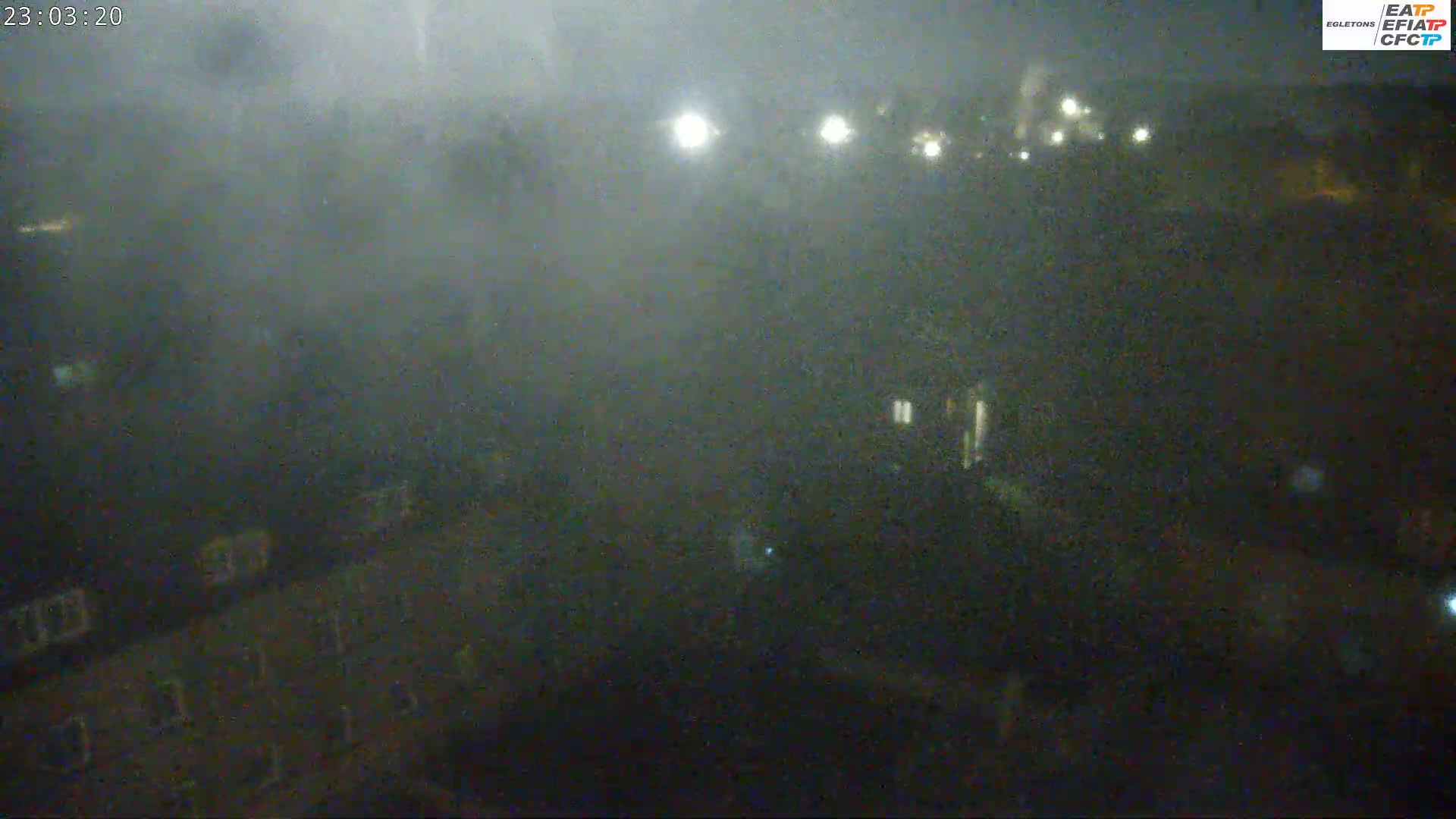 A nighttime, foggy view shows indistinct buildings and lights in the distance.