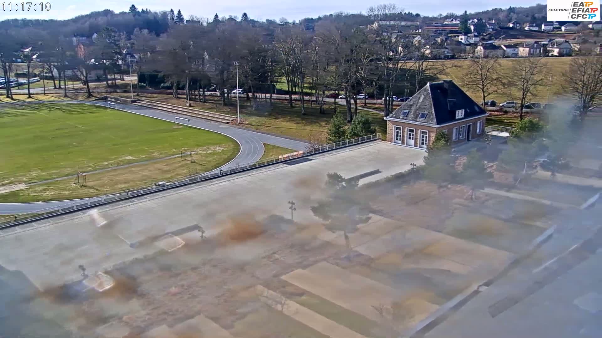 An aerial view shows a running track, a soccer field, and a small brick building on a sunny day.