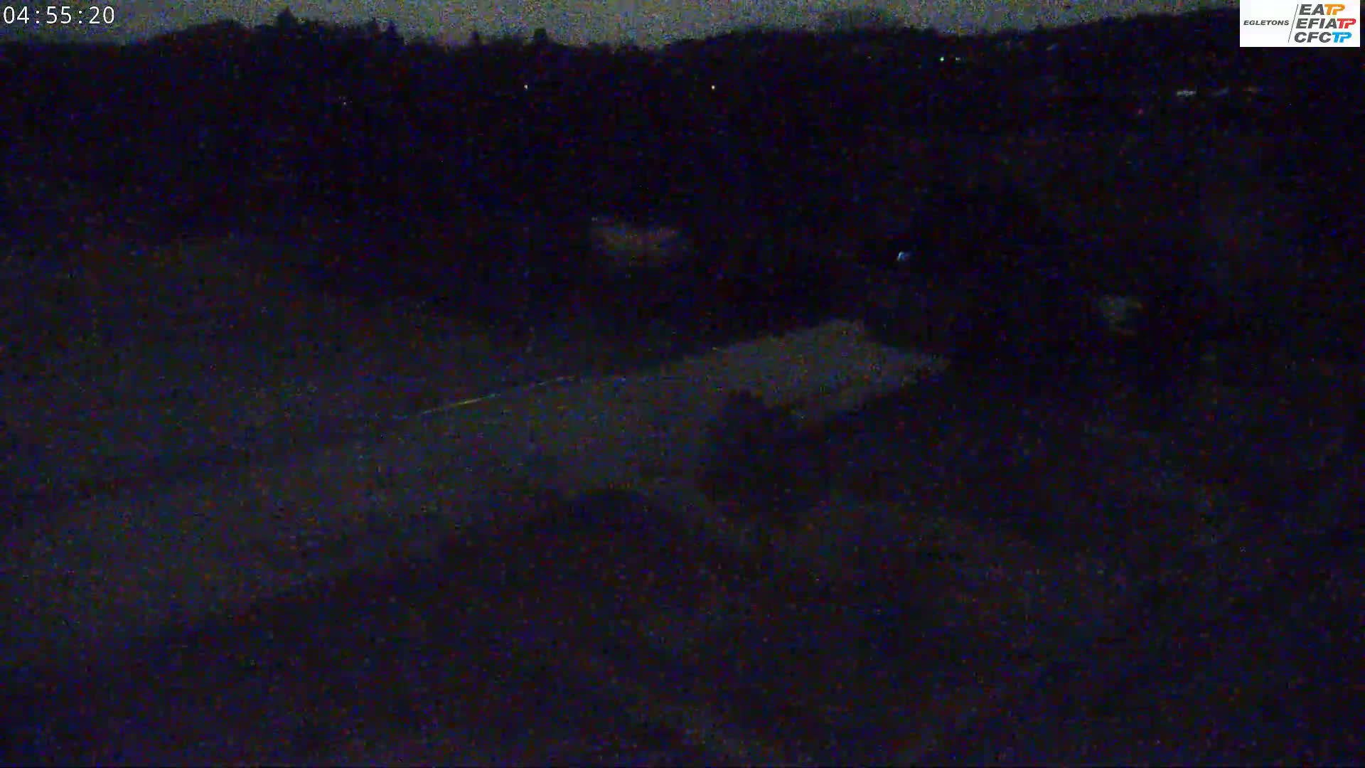 A dark, nighttime scene shows a road with faint vehicle lights and a dark, tree-covered hill in the background.