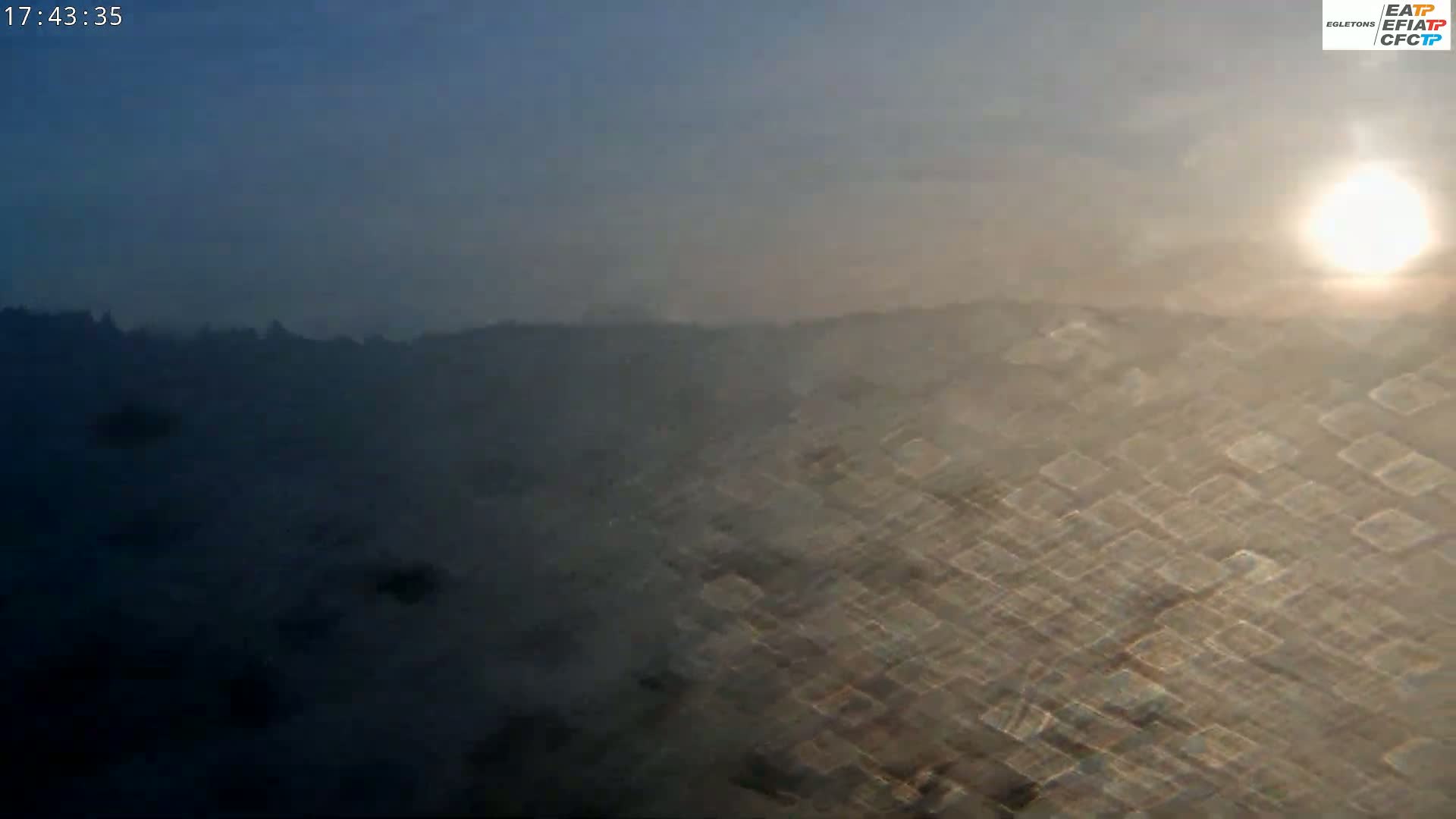 A hazy, sunlit view of a distant hilly landscape is seen through a textured surface.