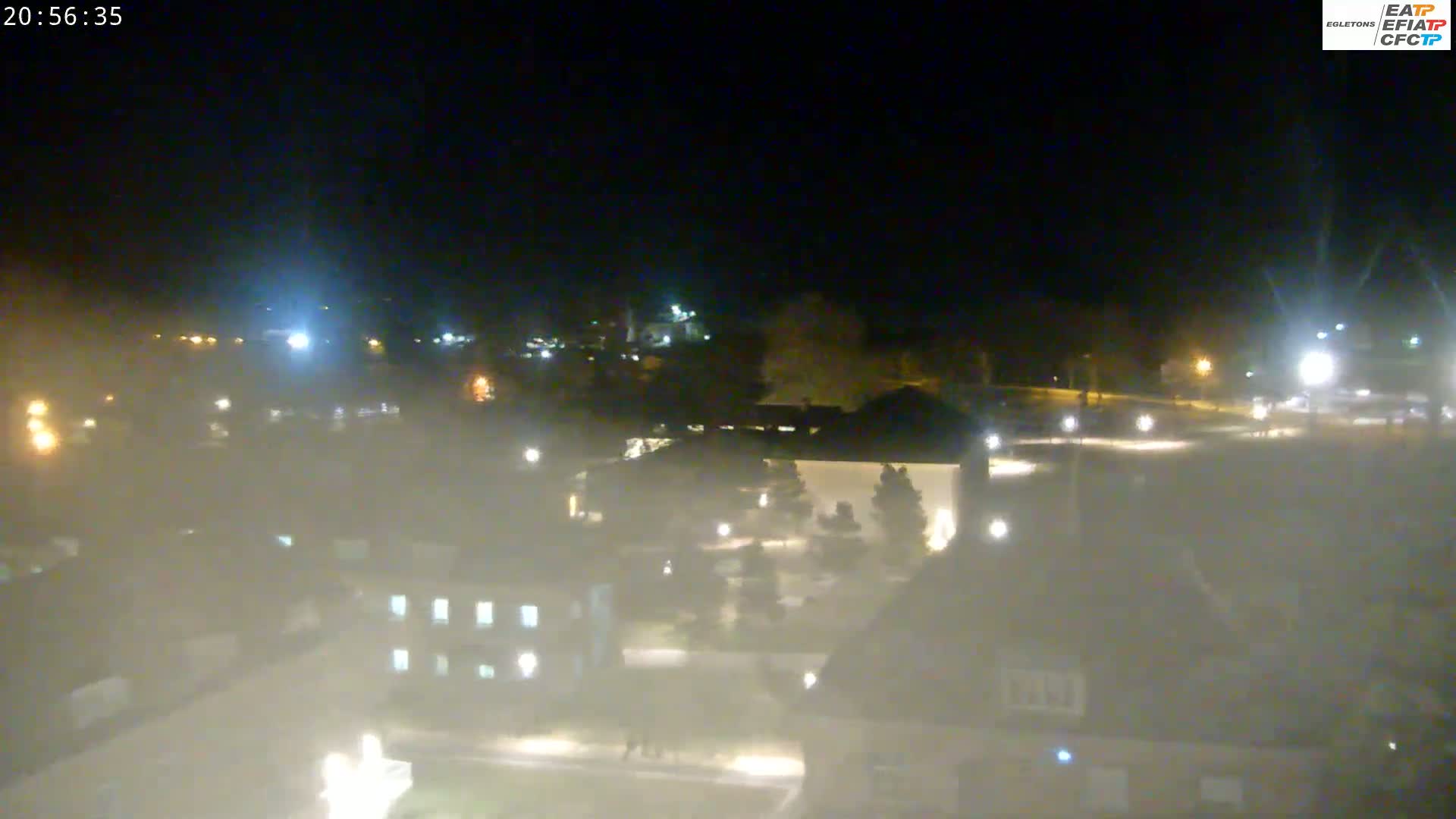 A hazy night scene shows a campus-like area with several buildings, trees, and scattered lights.