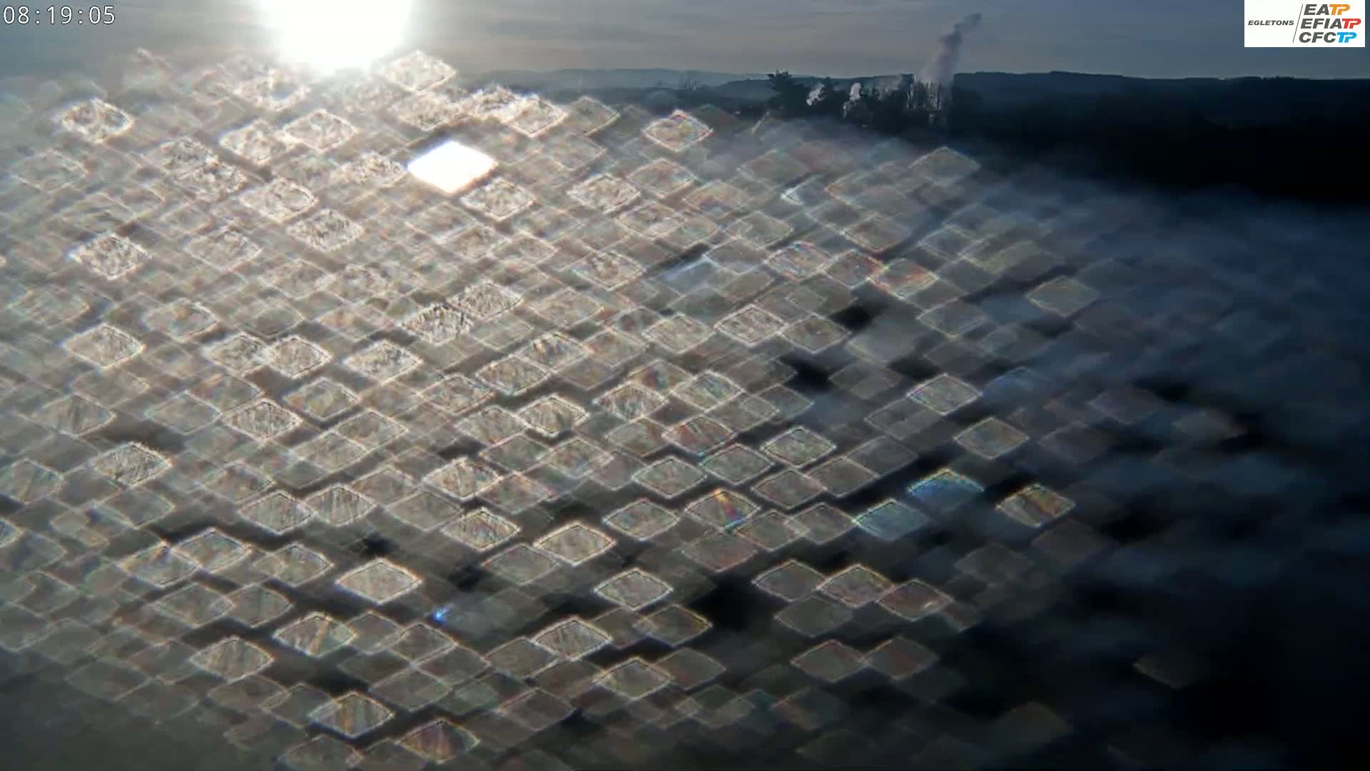 A diamond-patterned reflection of sunlight on a dark, possibly foggy, surface with a distant, hazy landscape visible in the background.