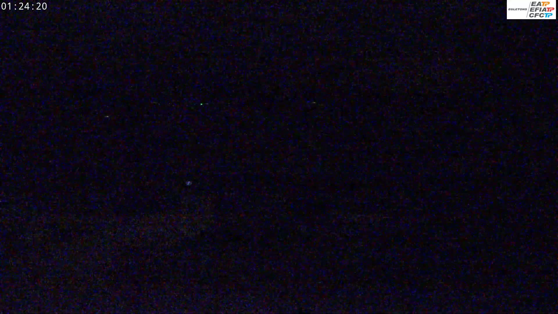 A dark, nighttime scene with a few faint lights visible in the distance.
