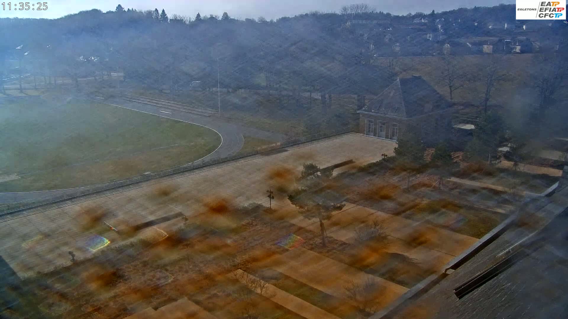 A hazy, high-angle view of a running track, a large building, and a landscaped area.