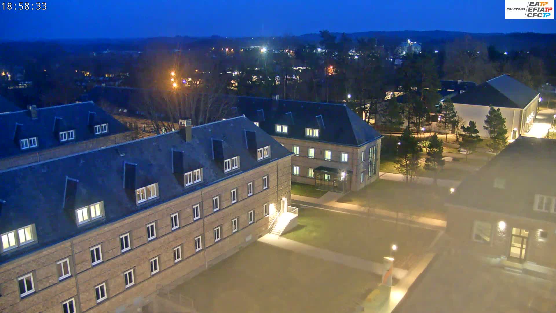A nighttime aerial view of a campus with several low-rise brick buildings, lit by streetlights under a dark blue sky.