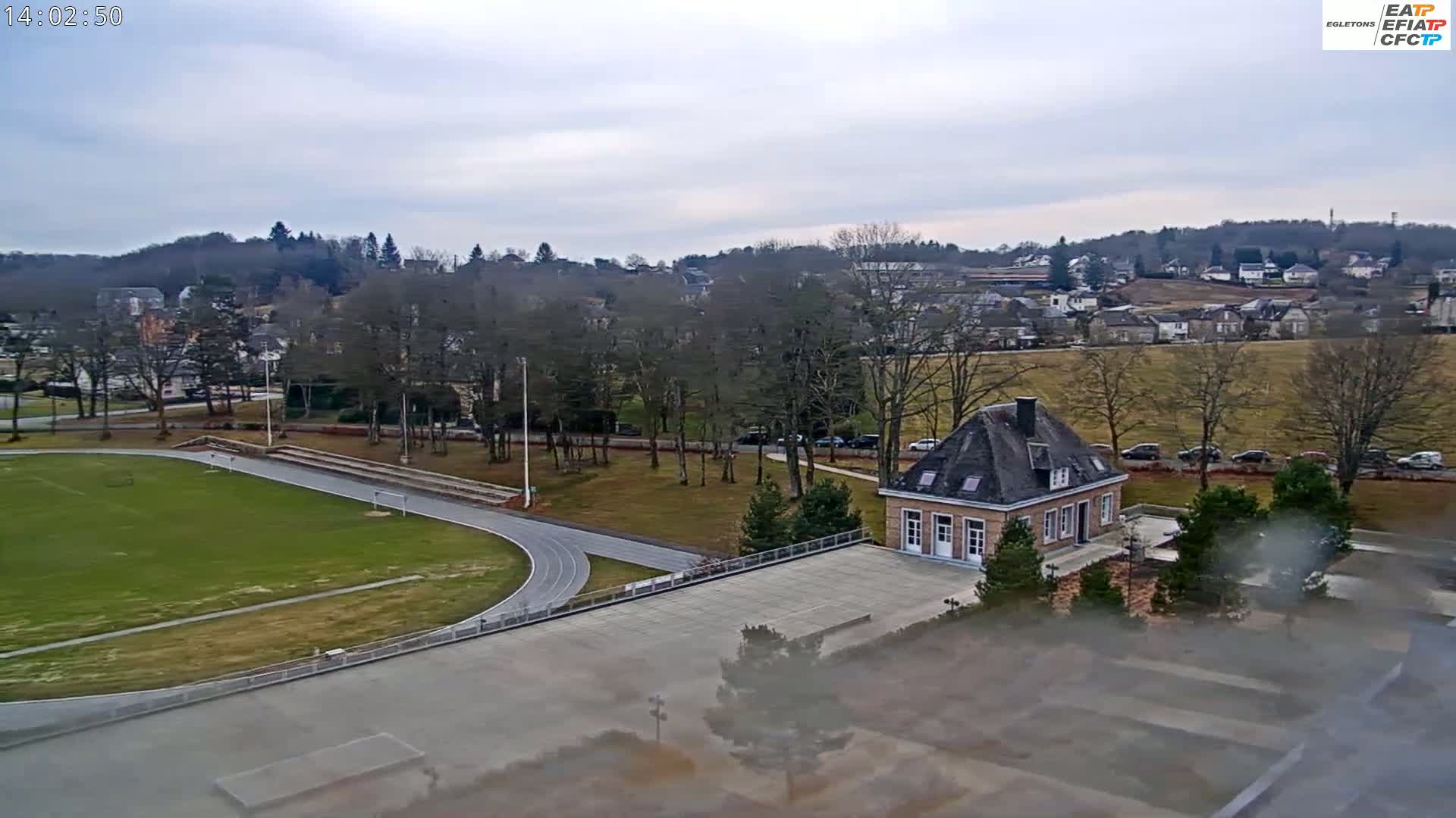 An overcast day reveals a running track and small building adjacent to a residential area nestled amongst bare winter trees and a grassy field.