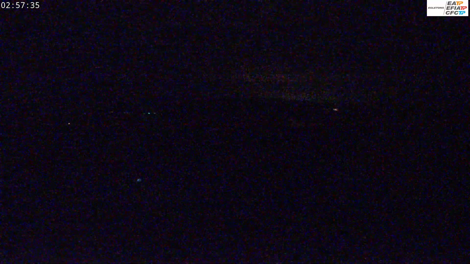 A nighttime, low-light view shows a dark, mostly featureless landscape with a few faint lights visible in the distance.