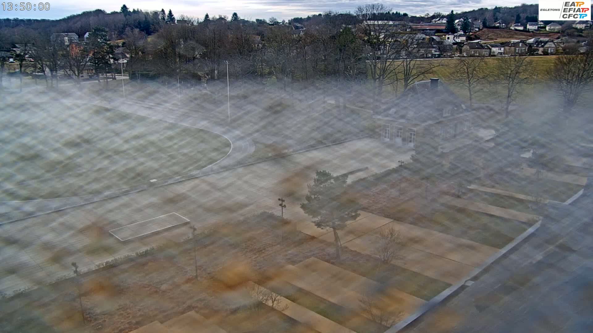 A high-angle view of a school campus with a running track, partially obscured by fog, showing a building and landscaping.