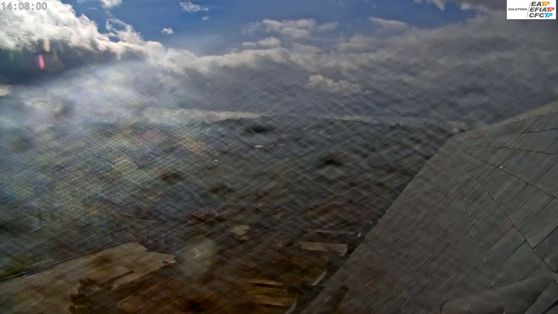 A partly cloudy sky overlooks a blurry, dark-colored landscape featuring a sloped, dark-gray roof in the bottom right corner.