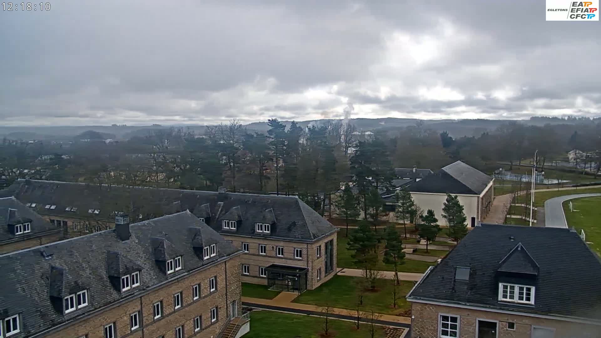 An aerial view shows several stone buildings on a campus with a grassy area and trees under an overcast sky.