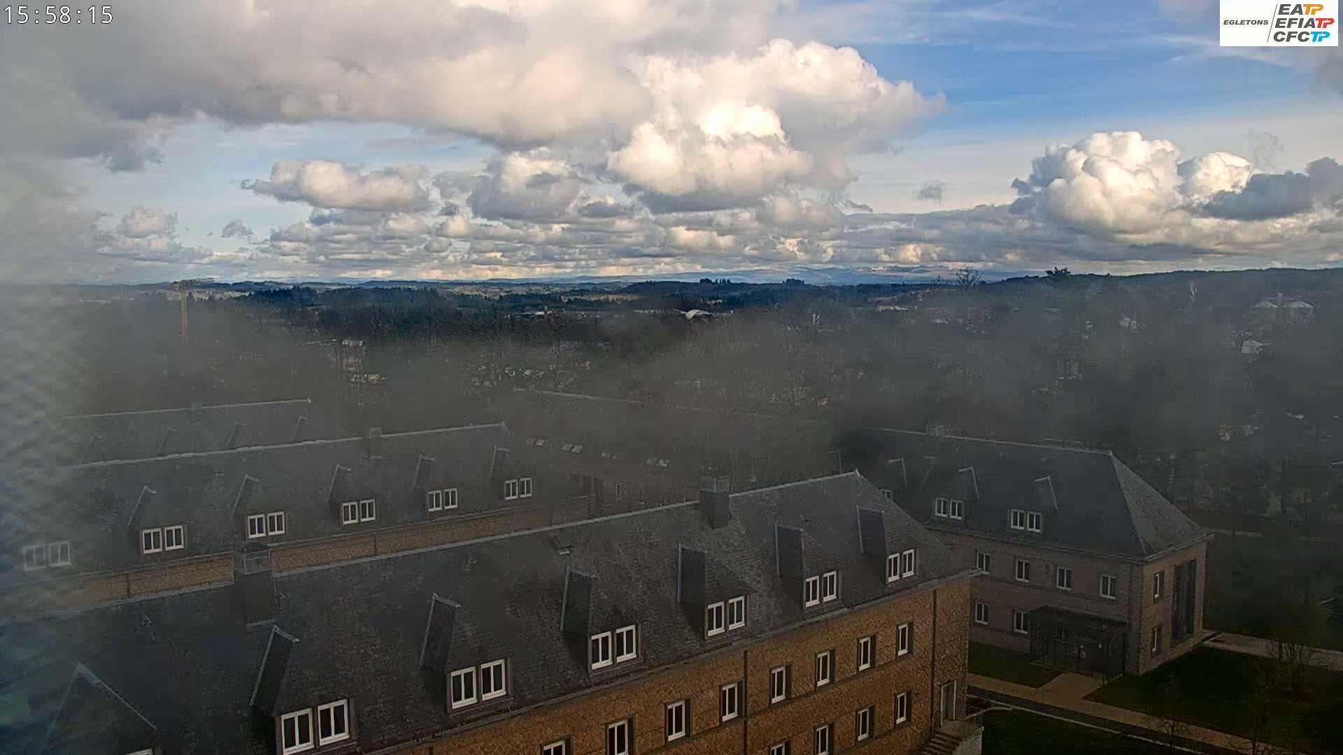 A hazy view of a sprawling campus with numerous buildings under a partly cloudy sky.
