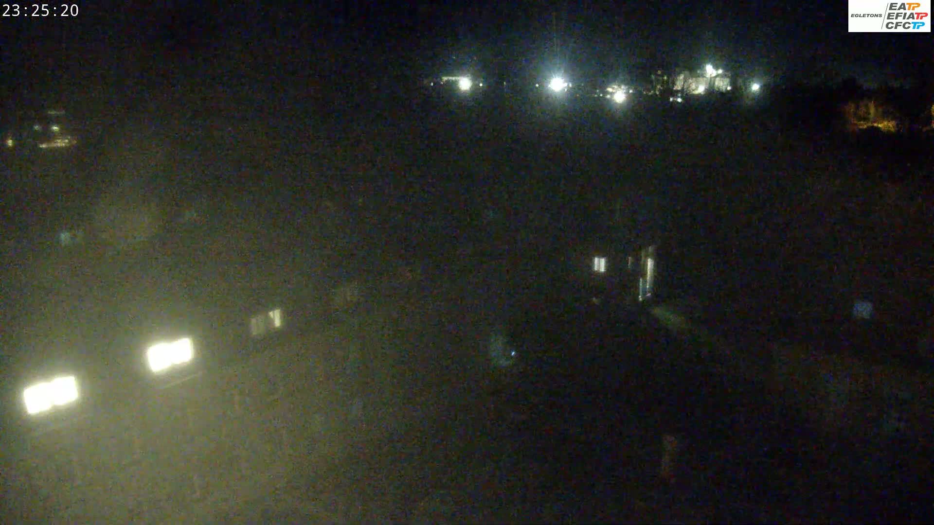 A nighttime, hazy view shows dimly lit buildings and vehicle headlights in the distance.