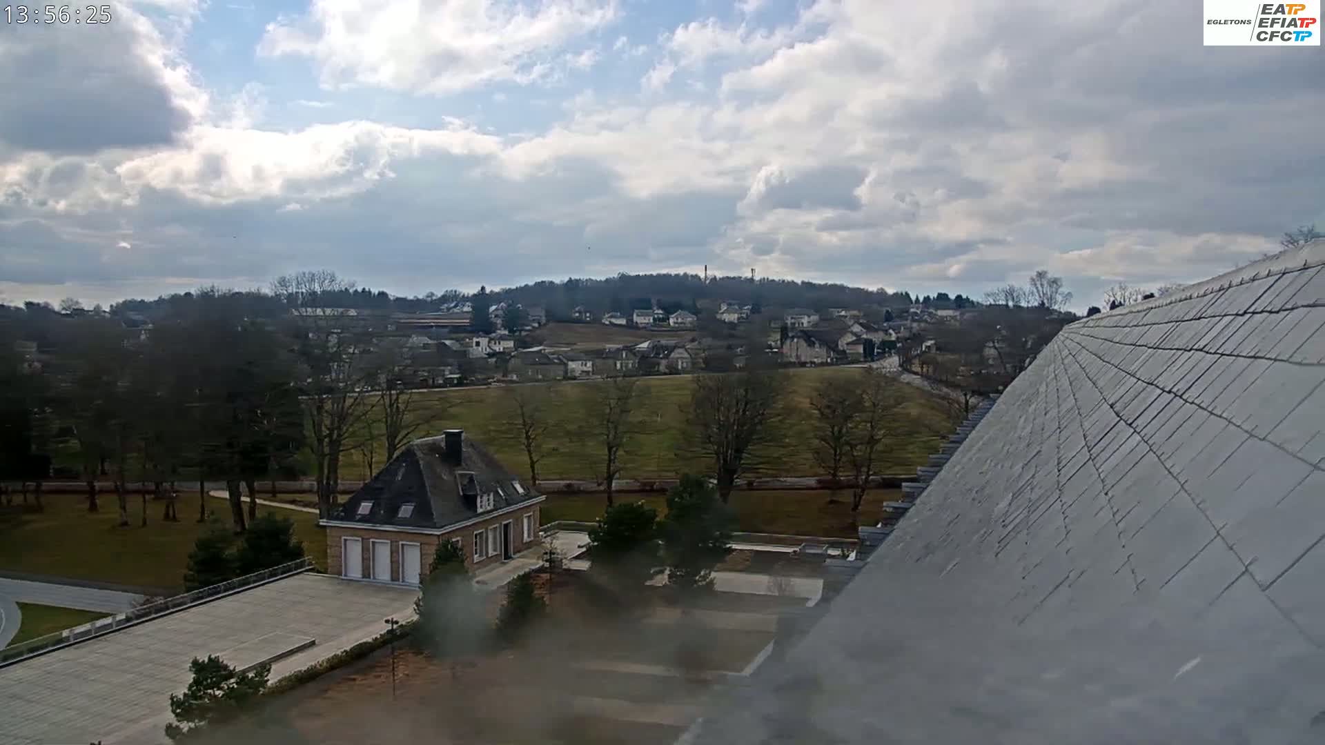 A partly cloudy sky overlooks a small town and a large house with a slate roof in the foreground.