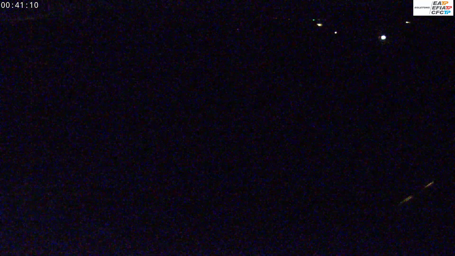 A nighttime, dark image shows a few distant lights on a dark horizon.