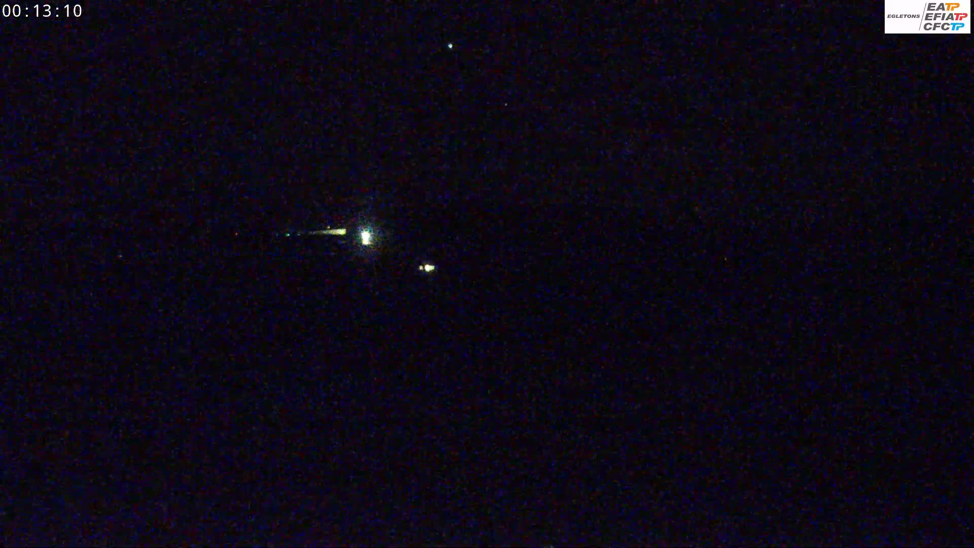 A dark, nighttime scene shows a few faint lights in the distance under a clear sky.