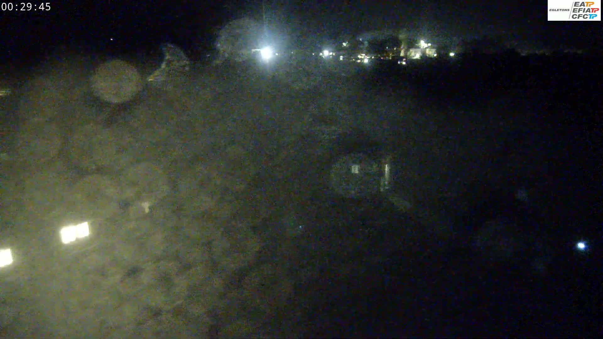 A nighttime, low-light view of a dark, indistinct landscape with a few distant lights visible.