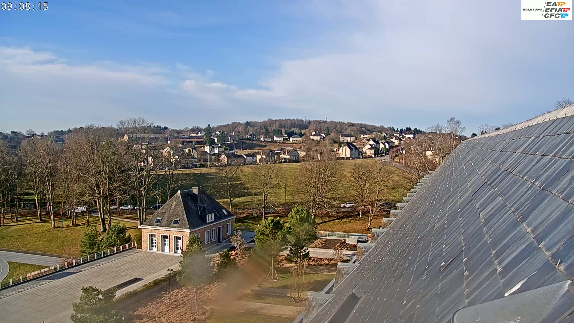 A mostly sunny day reveals a view of a town nestled in a valley, overlooked by a building with a steeply pitched slate roof.