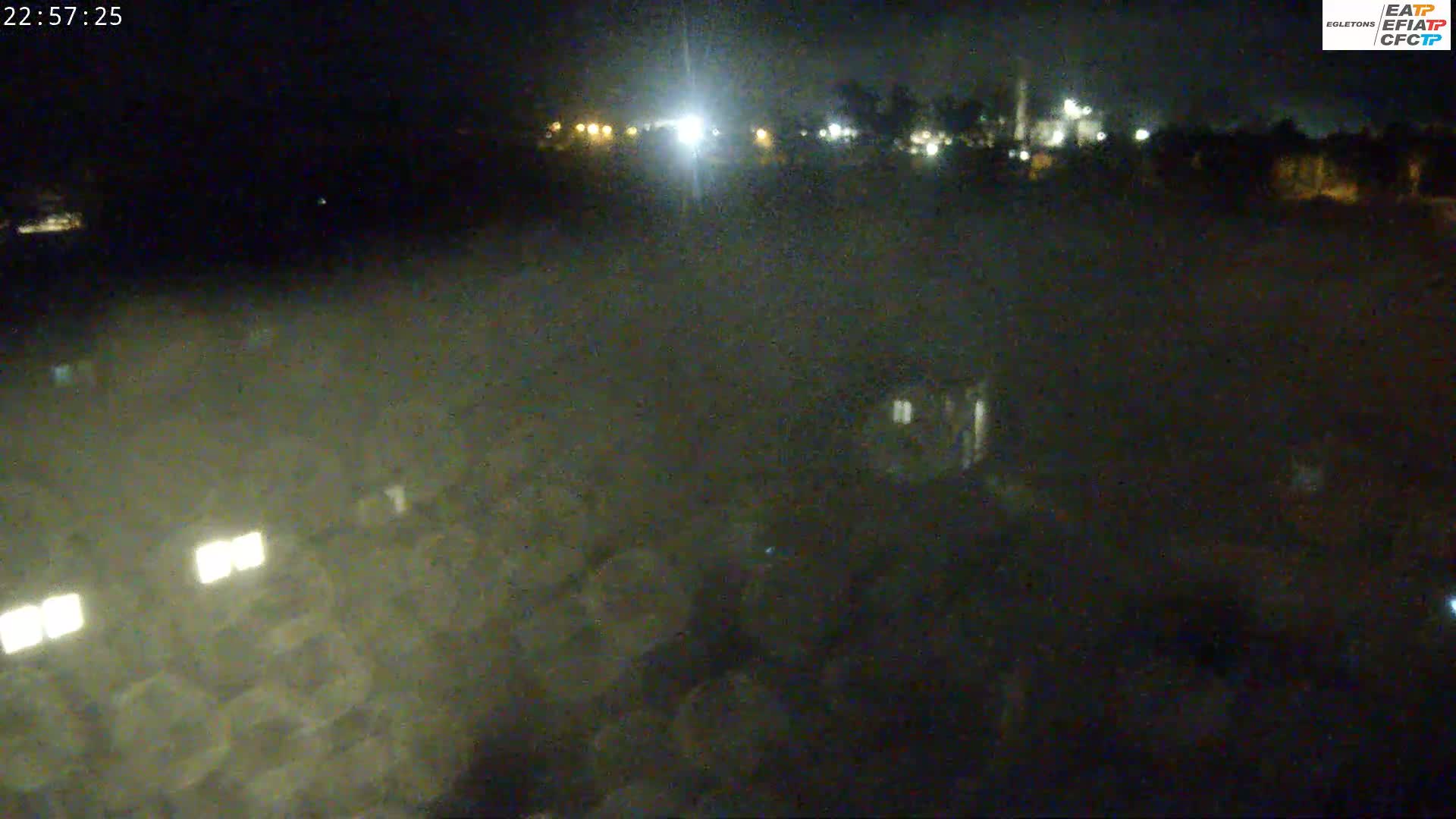A nighttime, low-light view of a dark, flat area with a few distant lights and some buildings barely visible in the hazy darkness.