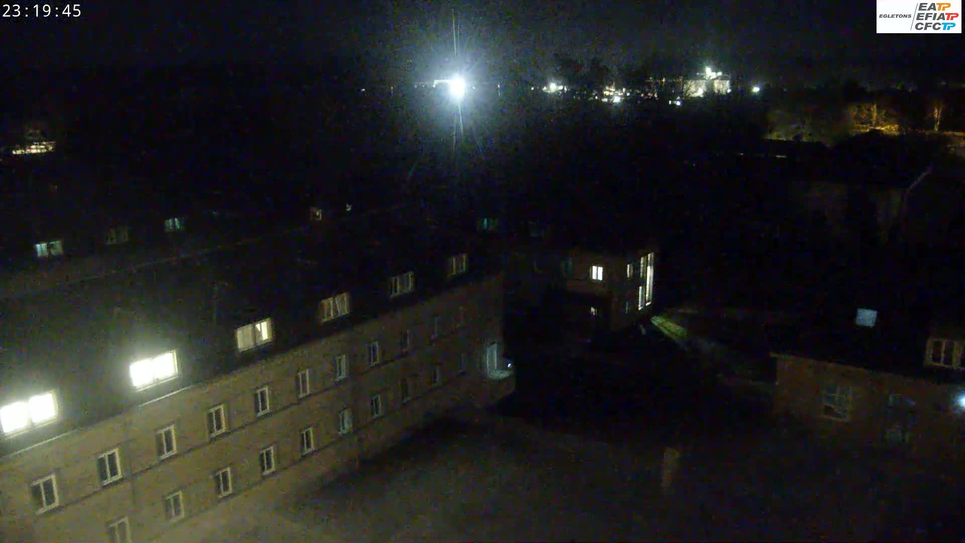 A nighttime aerial view shows several multi-story buildings with some illuminated windows, under a dark sky.
