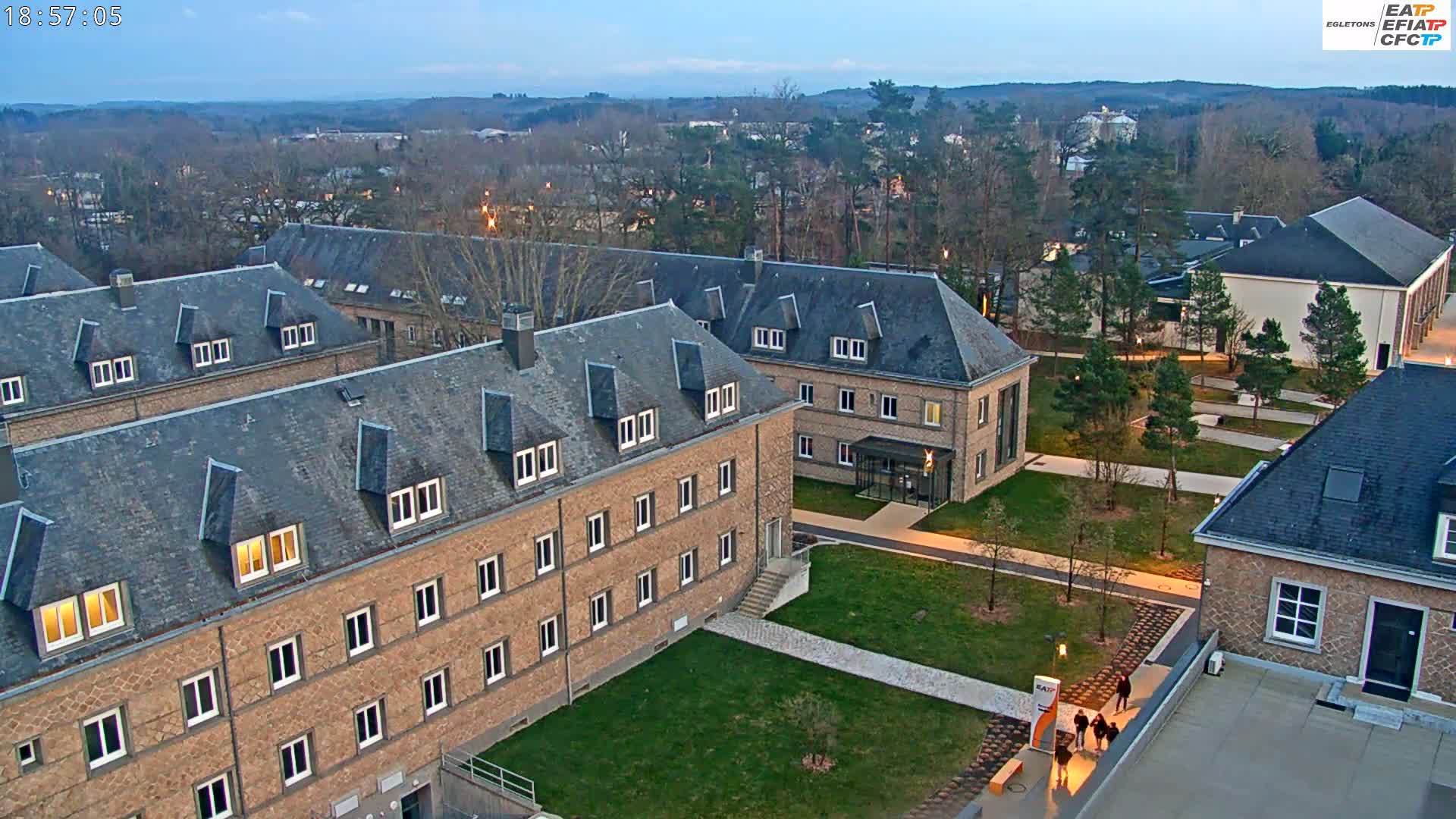 An aerial view of a campus at twilight shows several low brick buildings with slate roofs, surrounded by manicured lawns and walkways.