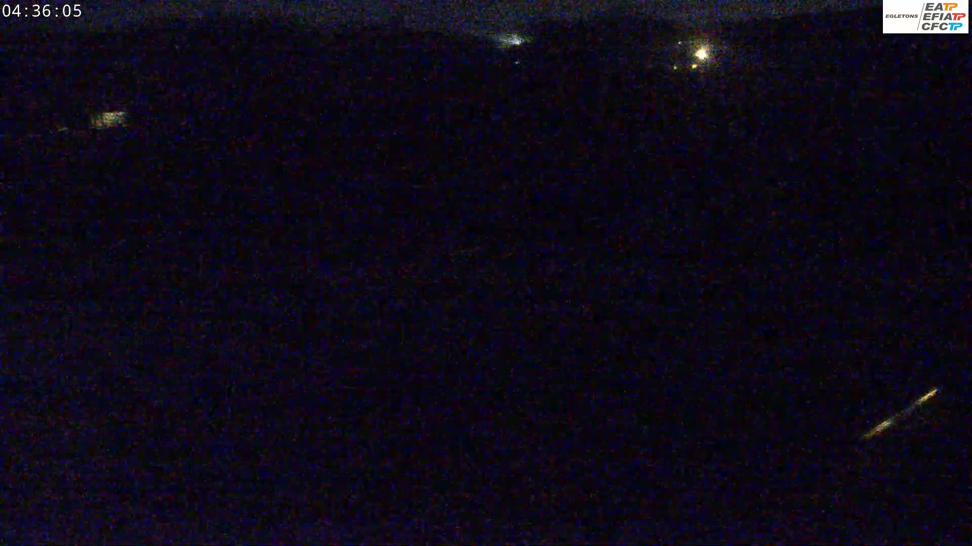 A nighttime long shot shows a dark, seemingly rural landscape with a few distant lights and a faint streak of light in the lower right corner.
