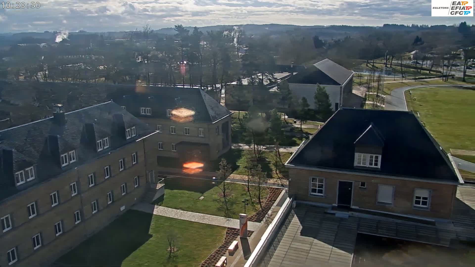 An aerial view of a campus with several buildings on a partly sunny day, showing a mix of landscaping and paved areas.