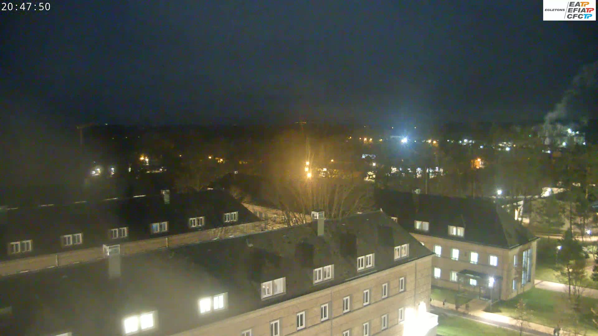 A nighttime aerial view of several buildings illuminated by artificial lights, surrounded by dark trees under a clear, dark sky.